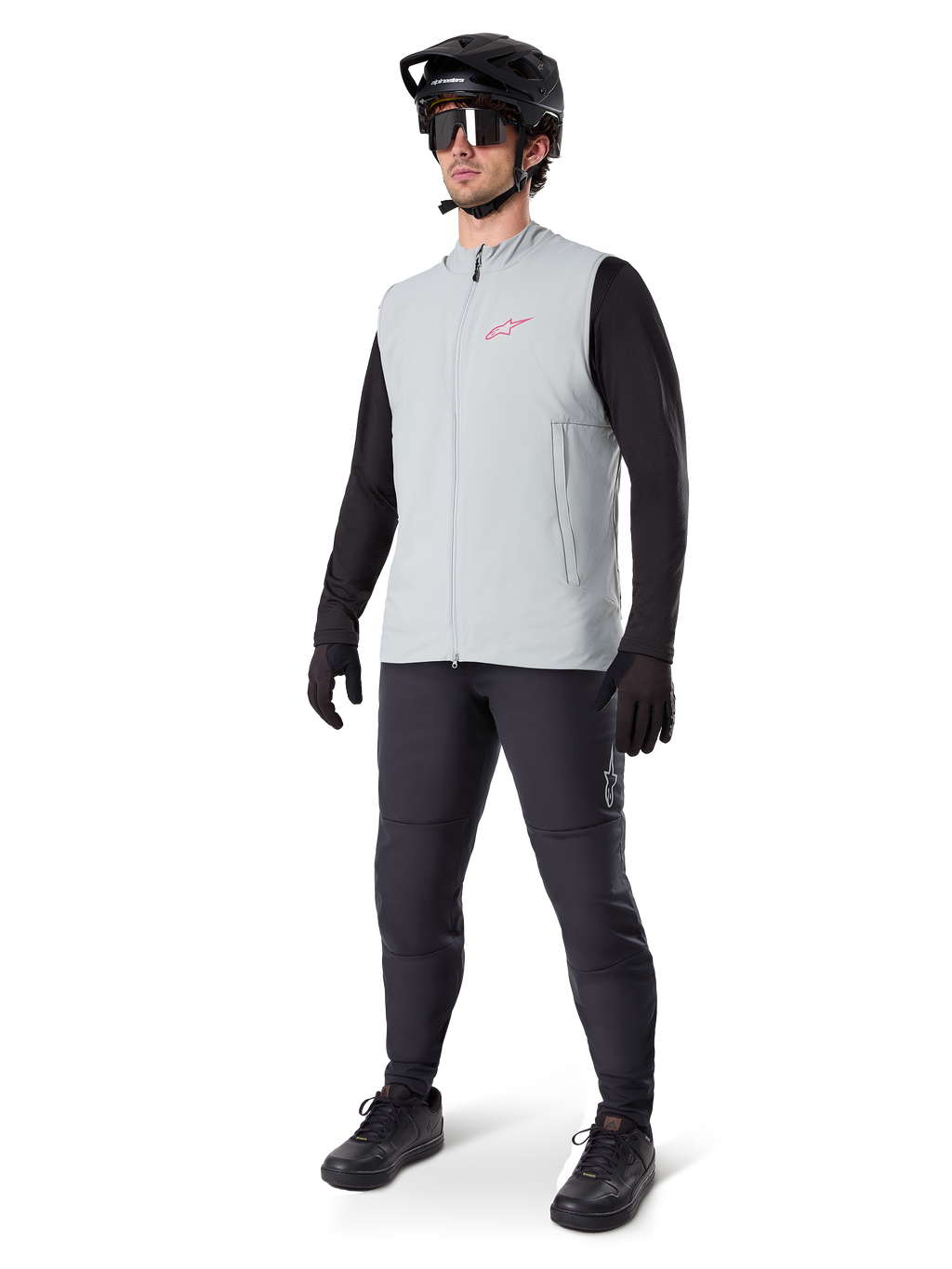 Gilet thermique Alpinestars A-Dura, gilet de cyclisme gris titane avec un logo rose, porté par un mannequin avec un maillot noir à manches longues, un pantalon gris foncé et un casque de VTT noir, équipement de performance pour rouler par temps froid