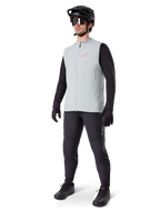 Gilet thermique Alpinestars A-Dura, gilet de cyclisme gris titane avec un logo rose, porté par un mannequin avec un maillot noir à manches longues, un pantalon gris foncé et un casque de VTT noir, équipement de performance pour rouler par temps froid