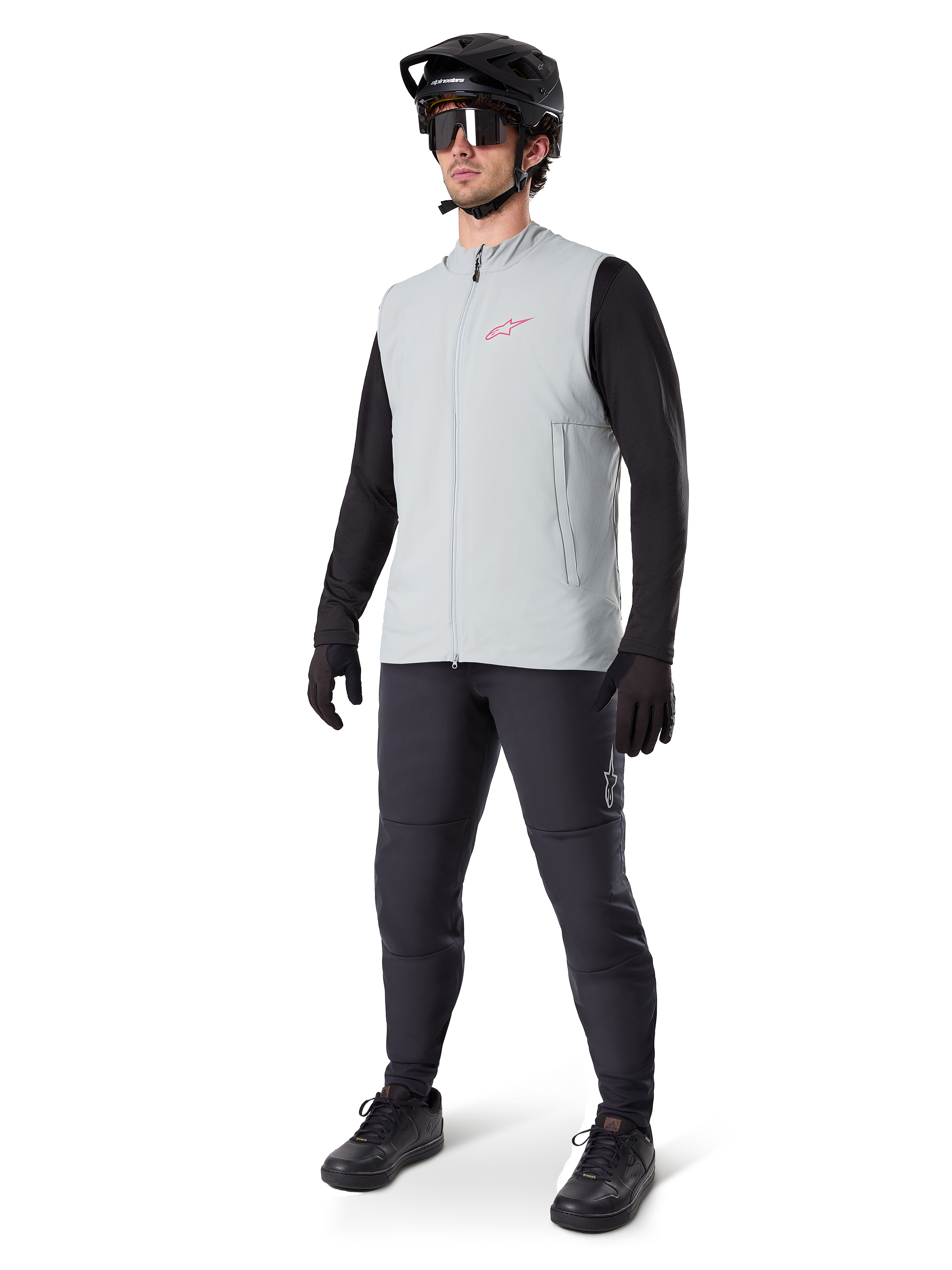 Gilet thermique Alpinestars A-Dura, gilet de cyclisme gris titane avec un logo rose, porté par un mannequin avec un maillot noir à manches longues, un pantalon gris foncé et un casque de VTT noir, équipement de performance pour rouler par temps froid