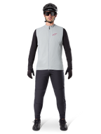 Gilet thermique Alpinestars A-Dura, gilet de cyclisme, gris titane, porté avec un maillot à manches longues noir et un pantalon noir, casque noir et lunettes de soleil, avec un logo Alpinestars rouge, isolation thermique légère pour le VTT