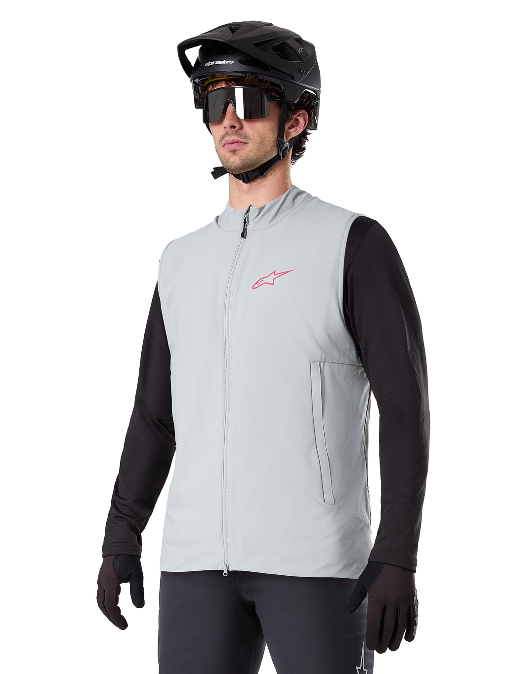 Gilet thermique Alpinestars A-Dura, gris titane, gilet de cyclisme isolant, porté sur un haut noir à manches longues avec un casque de VTT et des gants noirs, arborant un logo rose sur la poitrine et des poches latérales zippées verticales