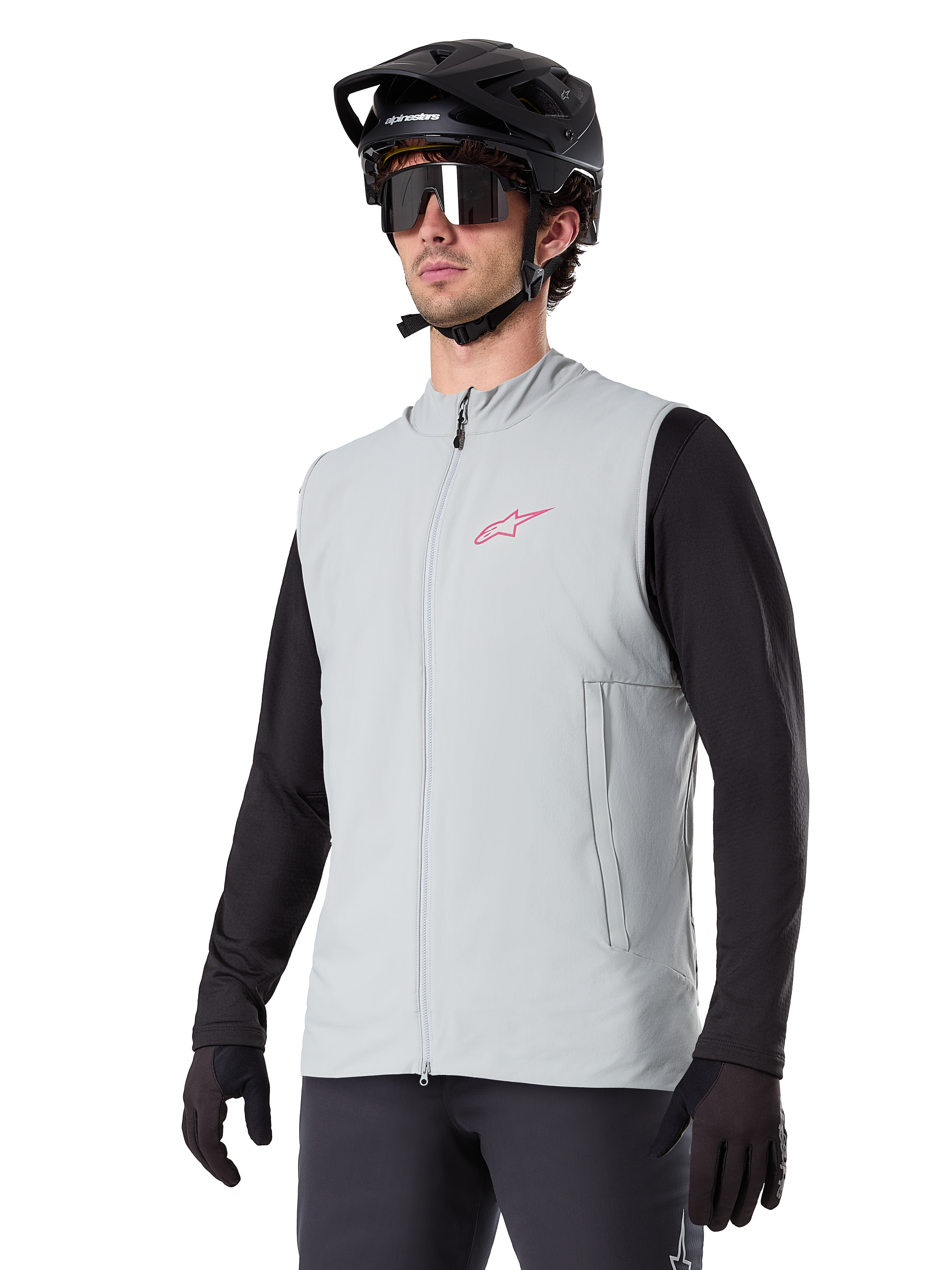 Gilet thermique Alpinestars A-Dura, gris titane, gilet de cyclisme isolant, porté sur un haut noir à manches longues avec un casque de VTT et des gants noirs, arborant un logo rose sur la poitrine et des poches latérales zippées verticales