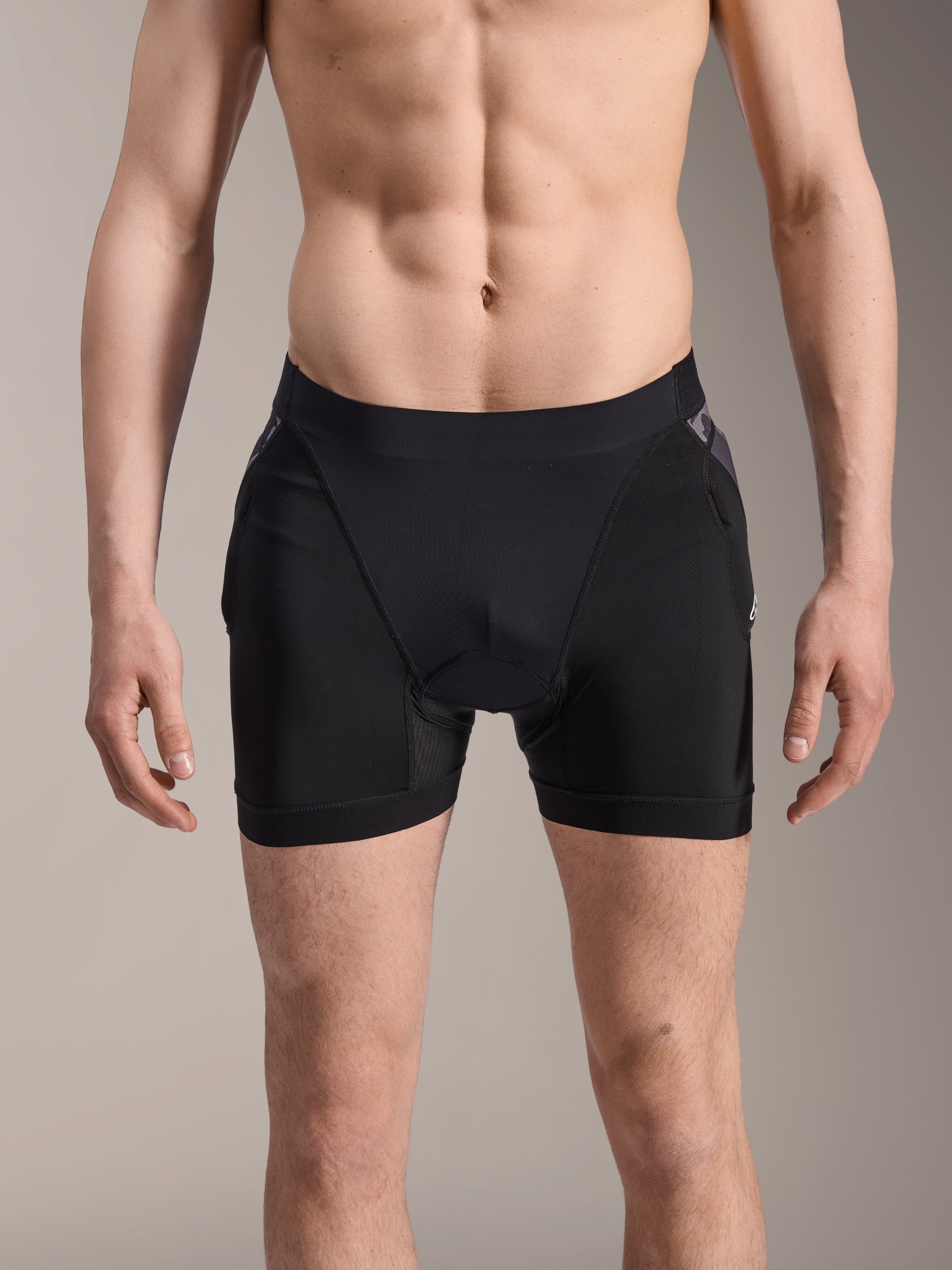 Boxer de Protection Alpinestars A-Motion Plasma, short de protection VTT, noir avec accents Camo noir, vue de face sur un modèle masculin, doté d'une maille extensible respirante et de protections de hanches intégrées pour la performance en cyclisme.