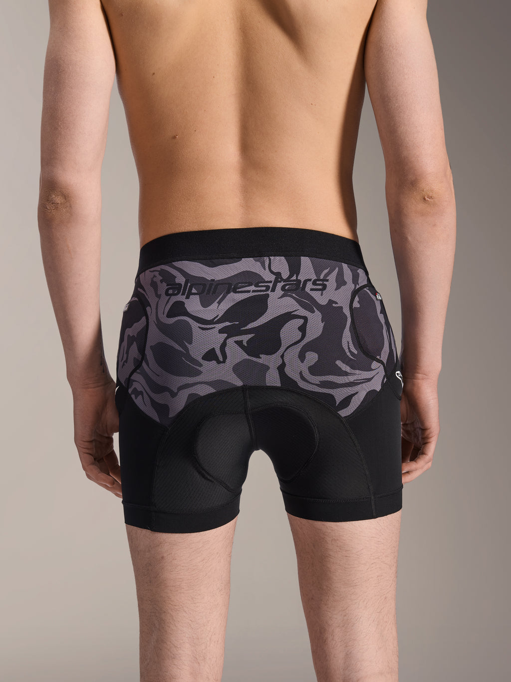 Alpinestars A-Motion Plasma Protection Boxers, short de protection VTT, Black Camo, vue arrière portée par un mannequin, logo Alpinestars sur empiècement en maille camouflage, peau de chamois intégrée et poches de protection des hanches, sous-couche respirante pour le cyclisme tout-terrain