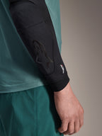 Alpinestars A-Motion Plasma Elbow Sleeve, coudière de protection VTT, noire, vue rapprochée portée sur le bras avec un maillot bleu sarcelle, logo Astars ton sur ton et marquage Nucleon Plasma, design en maille à profil fin pour le cyclisme tout-terrain
