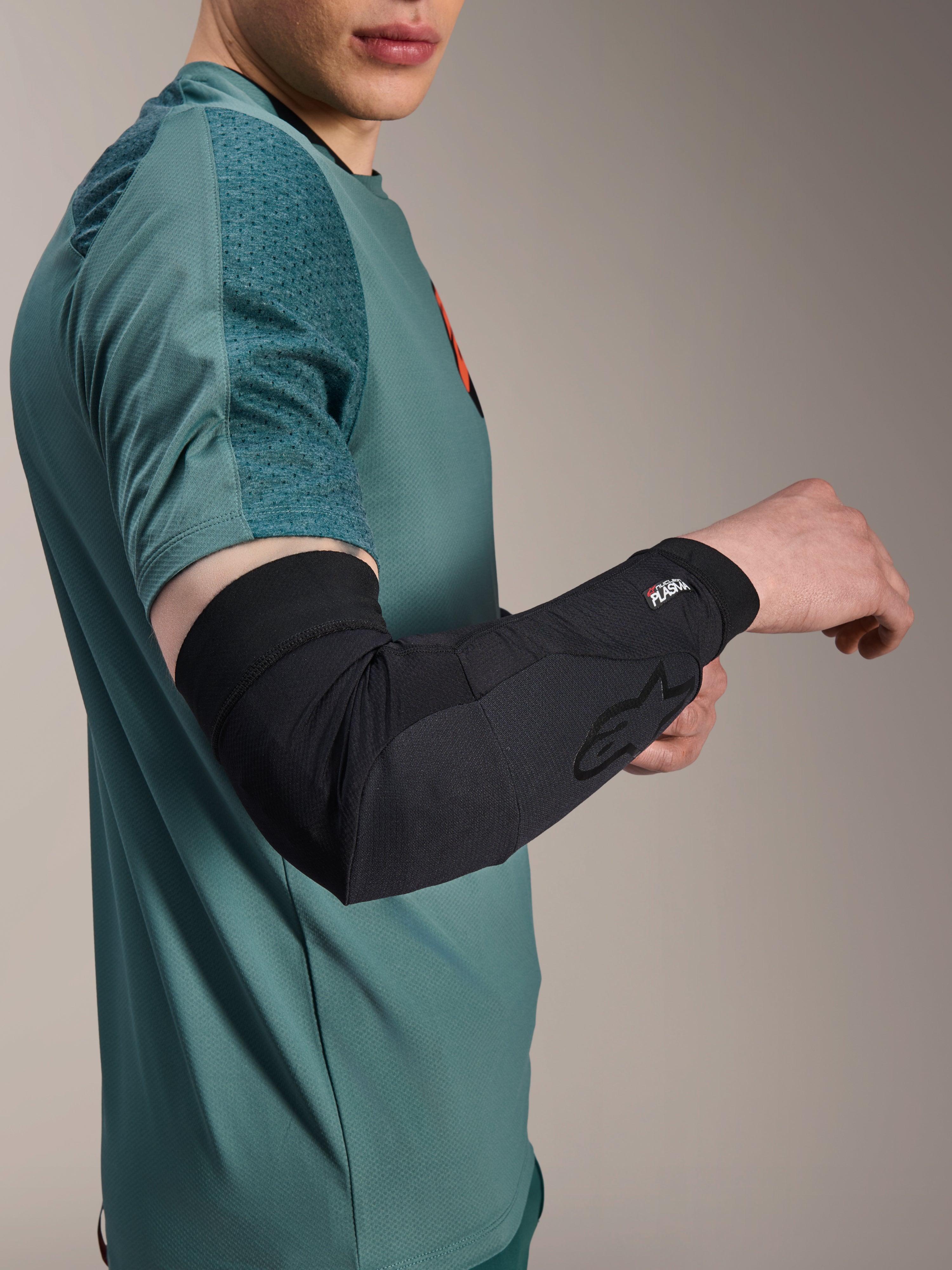 Alpinestars A-Motion Plasma Elbow Sleeve, protection de coude pour le cyclisme, noir, porté par un cycliste avec un maillot bleu sarcelle, arborant le logo Alpinestars et le marquage Nucleon Plasma, design épuré et respirant pour la protection VTT
