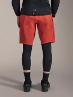 Alpinestars A-Motion Plasma Knee Sleeve, protections de genou VTT noires, vue de dos sous un short de VTT rouge avec un maillot noir et des chaussures de cyclisme techniques, équipement de protection pour le vélo tout-terrain
