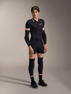 Mannelijk model in Alpinestars A-Motion Plasma Protection Jacket met korte mouwen, Black Camo met grijze schouders met patroon, centrale ritssluiting aan de voorzijde en wit logo op de borst, gedragen met zwarte arm- en kniebeschermers, technische MTB-beschermingsuitrusting voor off-road rijden.