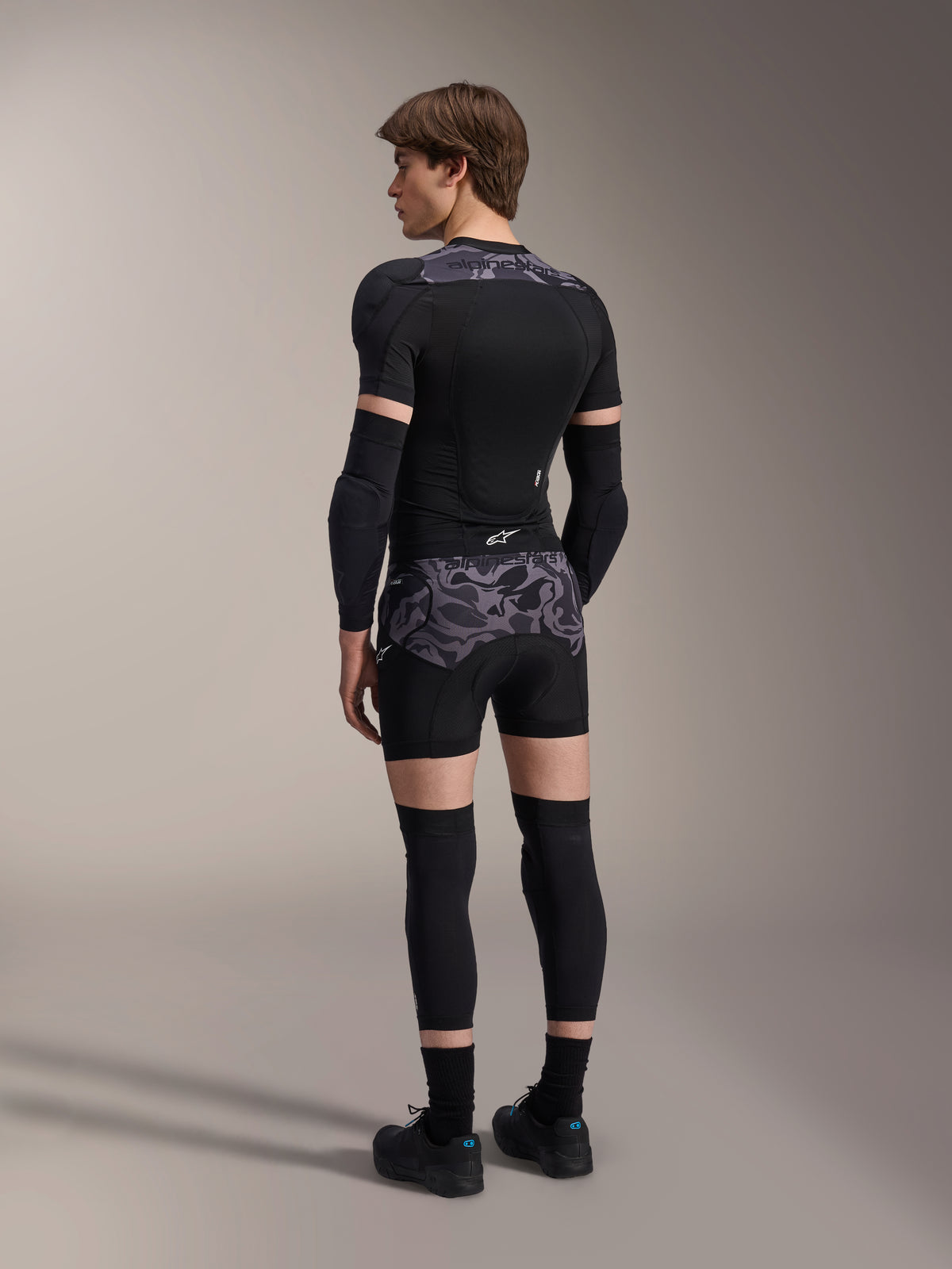 Mannequin portant le boxer de protection A-Motion Plasma Alpinestars en motif Black Camo et la veste de protection A-Motion Plasma assortie, vue de dos montrant le camouflage gris, les coudières, les genouillères et les chaussures de cyclisme, équipement de protection complet pour VTT.