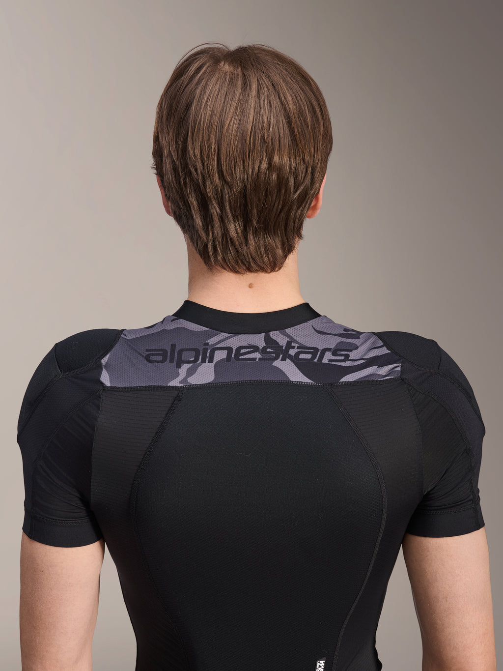 Alpinestars A-Motion Plasma Protection Jacket - korte mouwen, achteraanzicht van het bovenlichaam, zwart met grijs camouflagepaneel over de schouders met Alpinestars-logo, ademende stretch mesh-constructie voor MTB-bescherming