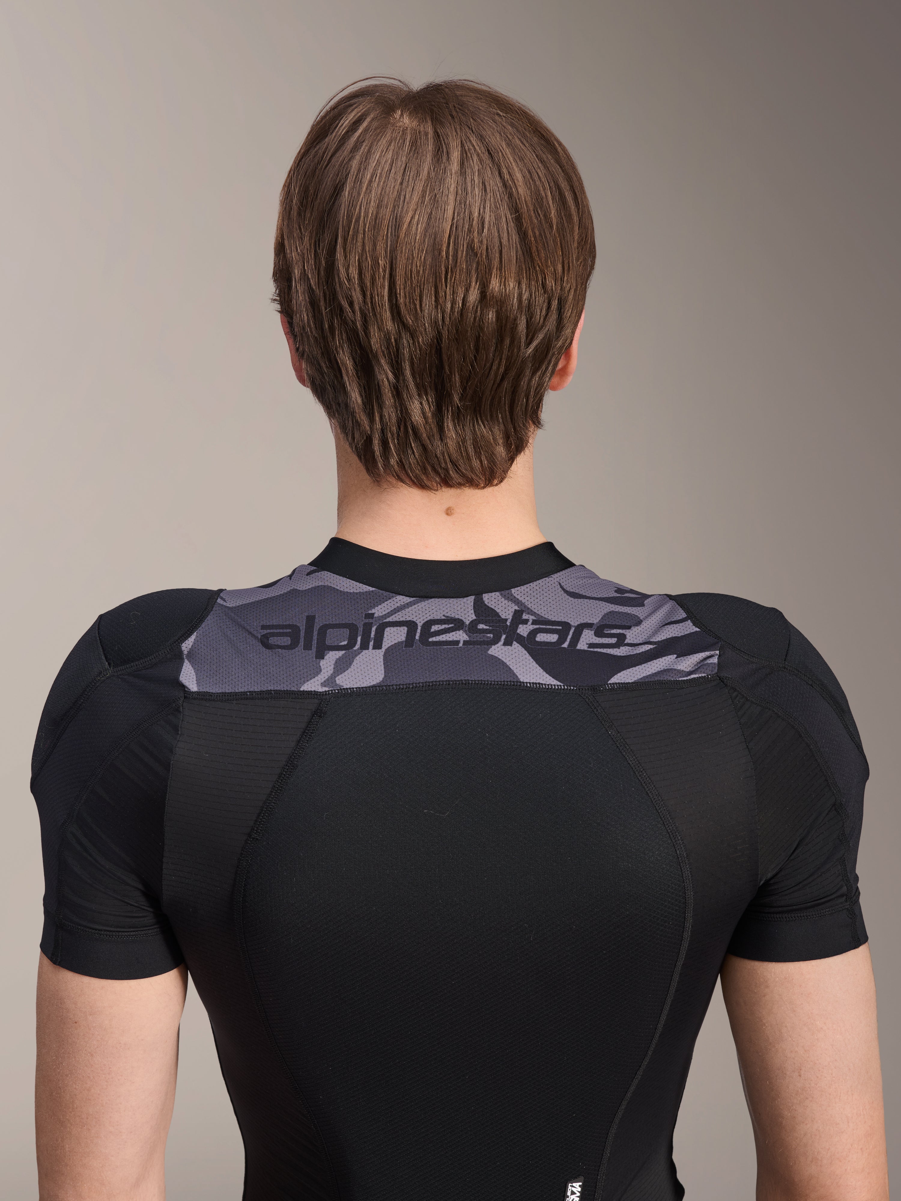 Alpinestars A-Motion Plasma Protection Jacket - korte mouwen, achteraanzicht van het bovenlichaam, zwart met grijs camouflagepaneel over de schouders met Alpinestars-logo, ademende stretch mesh-constructie voor MTB-bescherming