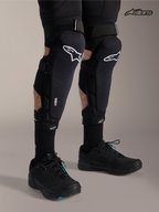 Alpinestars A-Impact Plasma Pro knie-/scheenbeenbeschermers, mountainbike kniebeschermers in zwart met wit logo, gedragen door een model met drievoudig sluitsysteem en Nucleon Plasma bescherming