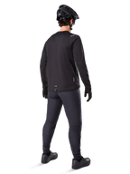 Pantalon thermique Alpinestars A-Dura, pantalon de VTT, noir, vu de dos, porté avec un maillot à manches longues assorti, un casque de VTT noir et des gants, équipement de cyclisme technique pour temps froid
