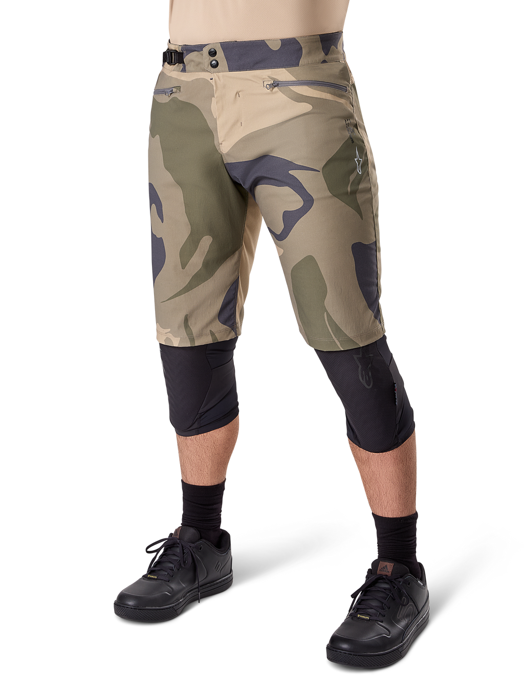 Alpinestars Short A-Dura Camo Liner, short de VTT, motif camouflage marron, vue de face montrant les poches zippées et les ajusteurs de taille latéraux, porté avec des genouillères noires et des chaussures de cyclisme noires, équipement durable pour le VTT