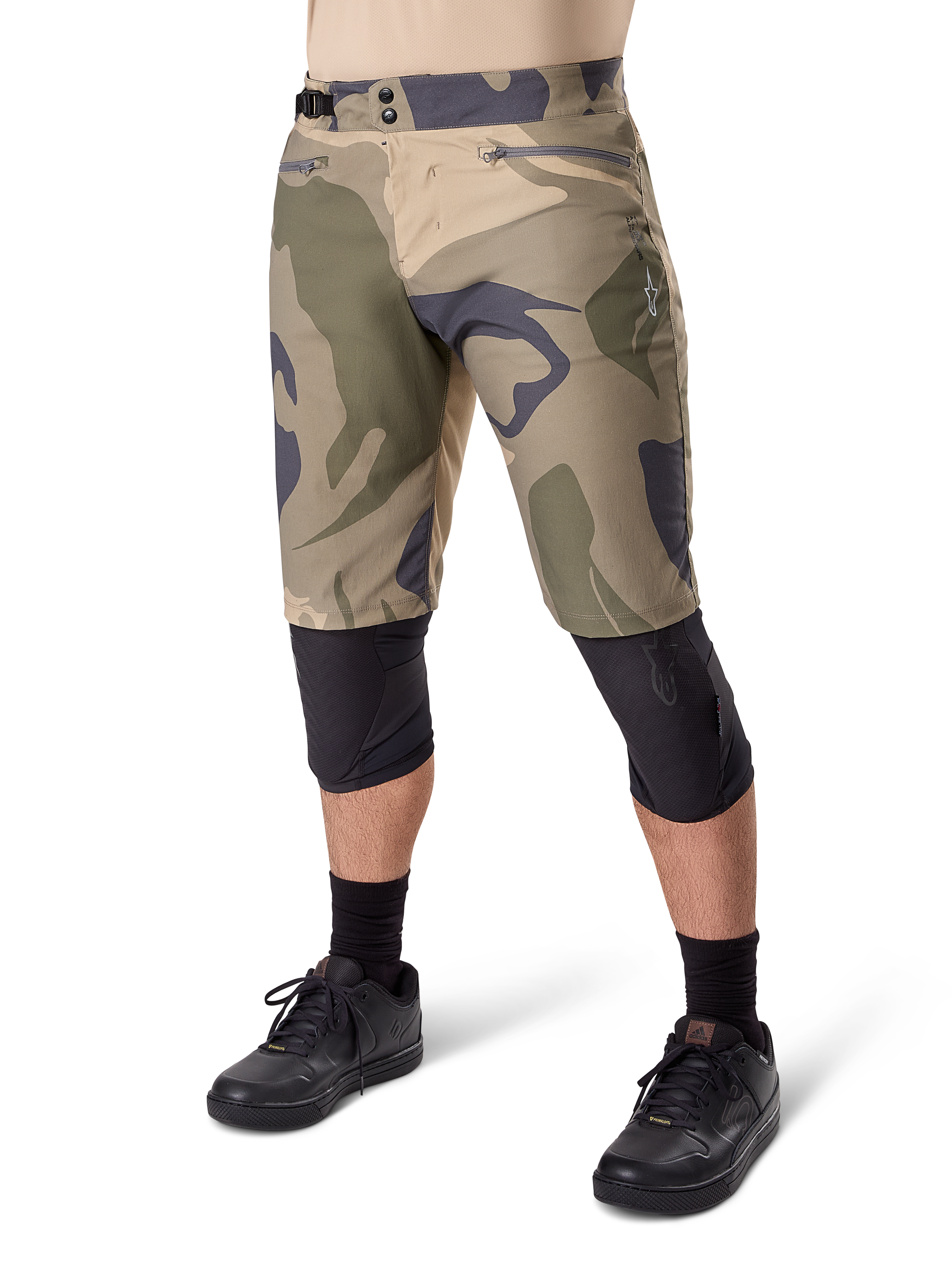 Alpinestars Short A-Dura Camo Liner, short de VTT, motif camouflage marron, vue de face montrant les poches zippées et les ajusteurs de taille latéraux, porté avec des genouillères noires et des chaussures de cyclisme noires, équipement durable pour le VTT