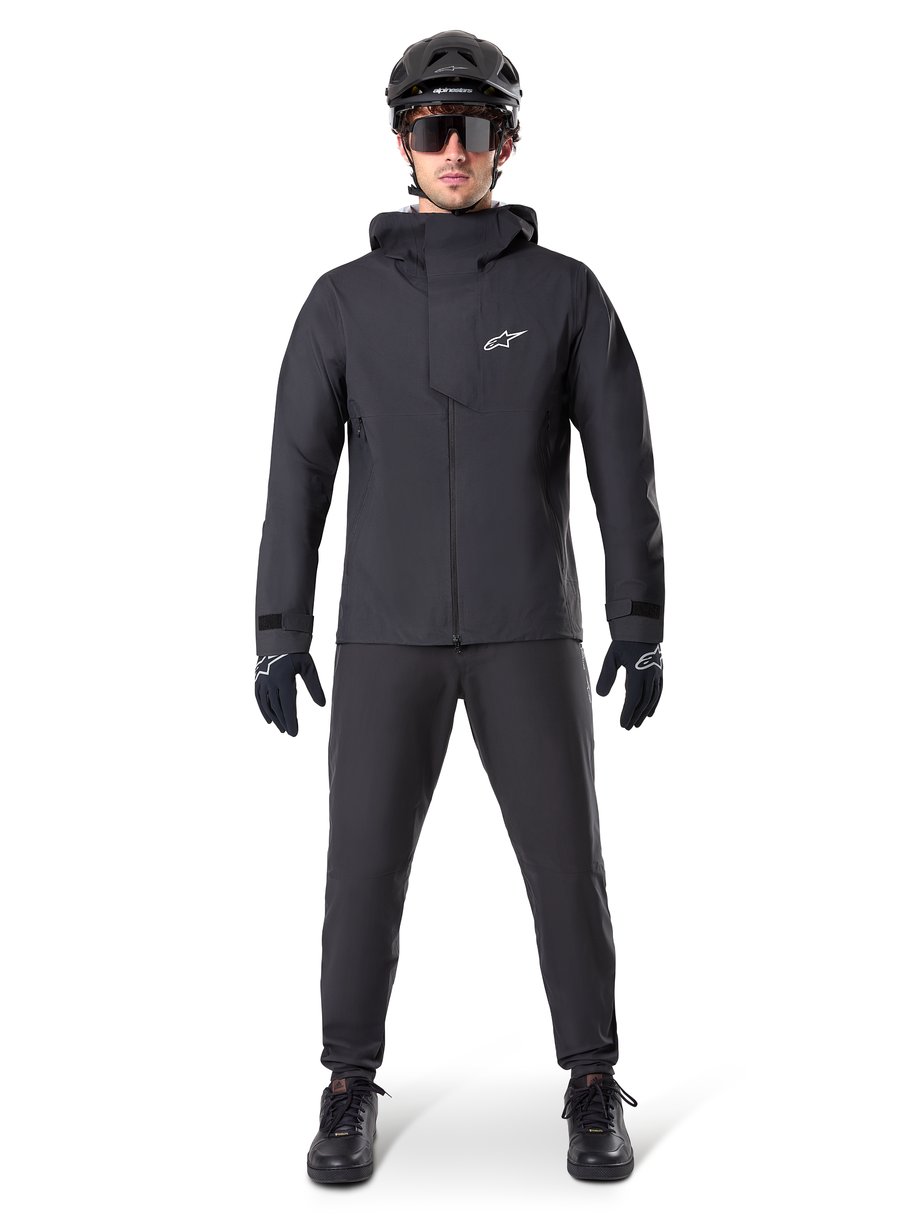 Pantalon imperméable Alpinestars A-Dura, pantalon de VTT noir, porté avec un équipement de VTT complet noir incluant une veste technique imperméable, un casque noir, des lunettes de soleil et des gants, conçu pour le tout-terrain par temps humide.