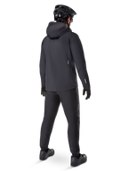Pantalon imperméable Alpinestars A-Dura, pantalon de VTT, noir, vue de dos sur un cycliste portant une tenue de VTT noire complète avec une veste à capuche et un casque, équipement imperméable durable pour les sentiers boueux