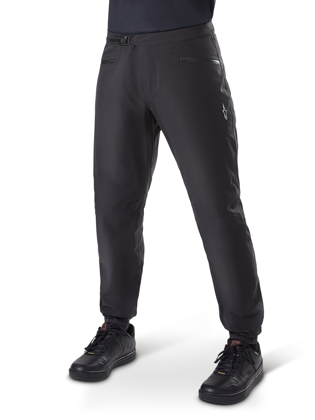 Pantalon imperméable Alpinestars A-Dura, pantalon de cyclisme VTT, noir, avec fermeture à cliquet à la taille, poches zippées et logo Astars blanc sur la cuisse, présenté porté avec des chaussures de vélo noires pour le trail par tous les temps