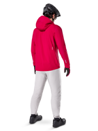 Pantalon imperméable Alpinestars A-Dura Titanium, vue arrière d'un cycliste portant un pantalon technique de VTT gris clair, veste à capuche rouge vif et casque noir, équipement imperméable durable pour le cyclisme par temps humide