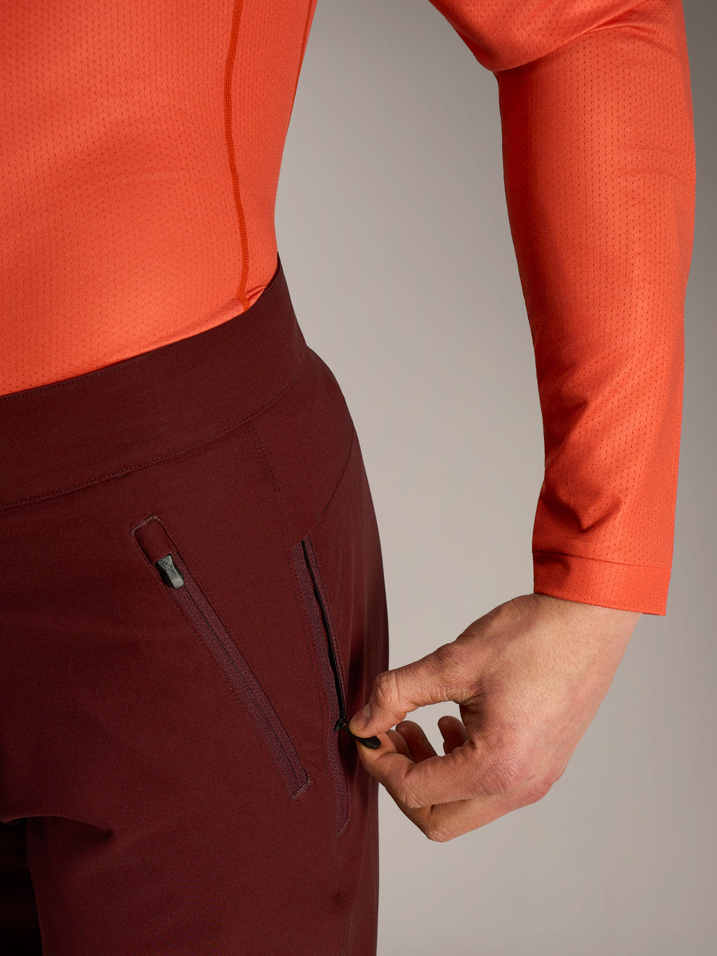 Alpinestars A-Dura Ride korte broek in bordeaux, detail van hand die de zijzak met ritssluiting en mesh-voering opent.