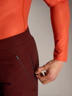 Alpinestars A-Dura Ride korte broek in bordeaux, detail van hand die de zijzak met ritssluiting en mesh-voering opent.