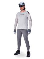 Pantalon Alpinestars A-Aria Elite, pantalon de VTT gris foncé, porté par un cycliste avec un maillot à manches longues gris clair et un casque gris, doté de ventilations découpées au laser sur les cuisses et d'une coupe performance ajustée pour le VTT