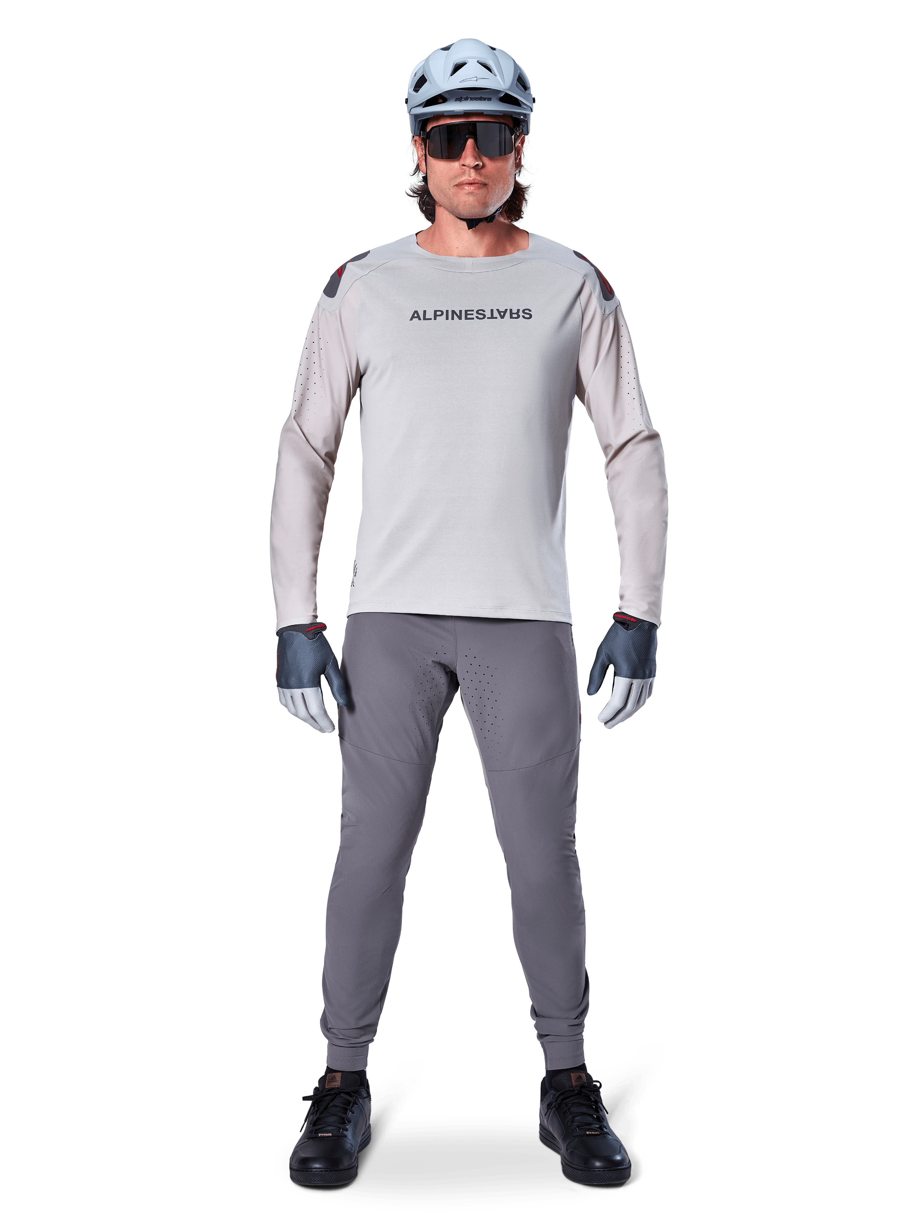 Pantalon Alpinestars A-Aria Elite, pantalon de VTT gris foncé, porté par un cycliste en maillot à manches longues gris clair, casque bleu clair et chaussures noires, doté de perforations laser visibles à l'intérieur des jambes et d'une coupe performance ajustée.