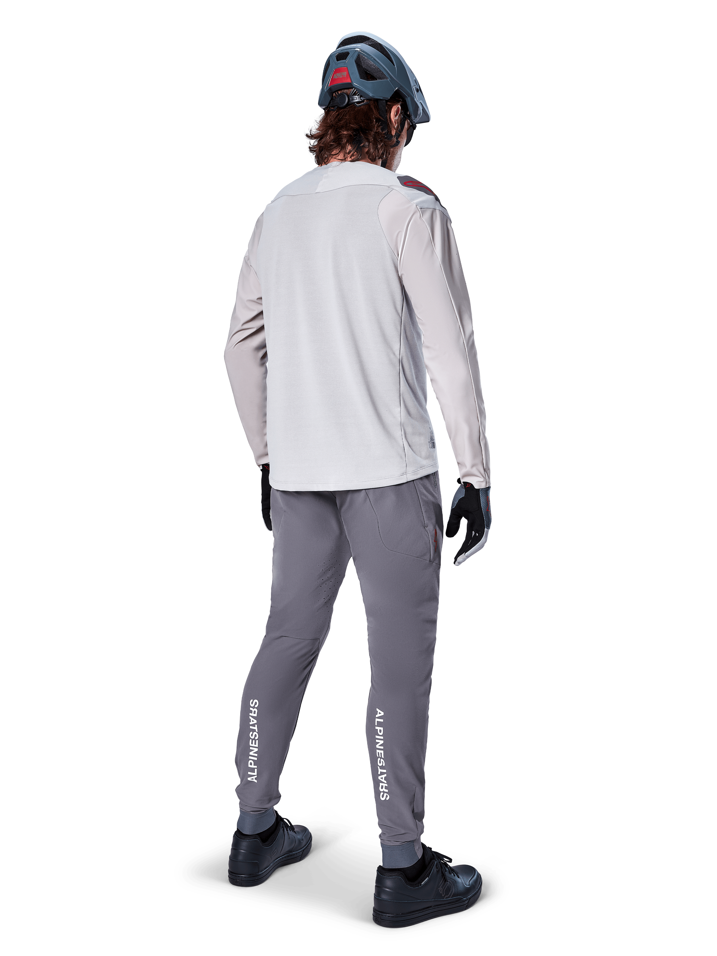 Pantalon Alpinestars A-Aria Elite, pantalon de cyclisme VTT, gris foncé, vue arrière d'un cycliste portant une tenue complète, logos Alpinestars blancs sur le bas des jambes, coupe performance avec perforations laser, associé à un maillot à manches longues gris clair et un casque de VTT gris