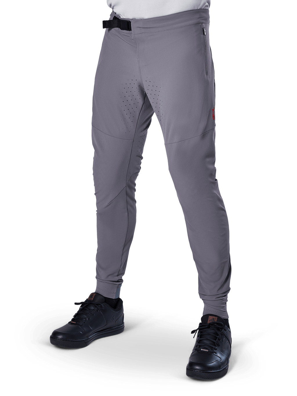 Alpinestars A-Aria Elite Pants, pantalon de VTT gris foncé, panneaux perforés au laser sur les cuisses, fermeture à boucle magnétique noire, poche zippée, détail de logo rouge, coupe performance ajustée, porté avec des chaussures noires