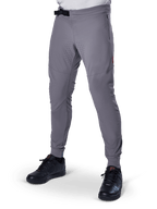 Alpinestars A-Aria Elite Pants, pantalon de VTT gris foncé, panneaux perforés au laser sur les cuisses, fermeture à boucle magnétique noire, poche zippée, détail de logo rouge, coupe performance ajustée, porté avec des chaussures noires