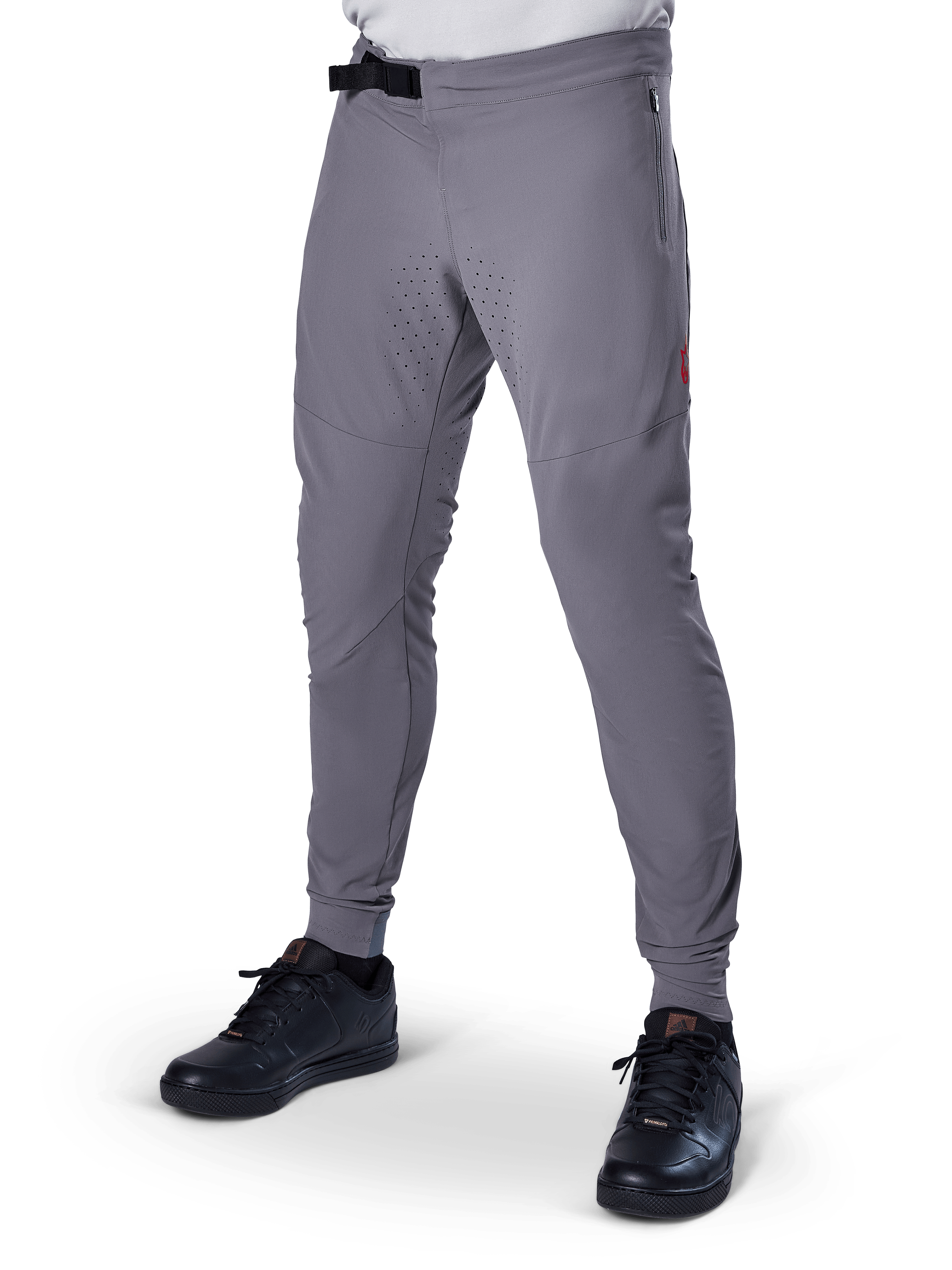 Alpinestars A-Aria Elite Pants, pantalon de VTT gris foncé, panneaux perforés au laser sur les cuisses, fermeture à boucle magnétique noire, poche zippée, détail de logo rouge, coupe performance ajustée, porté avec des chaussures noires