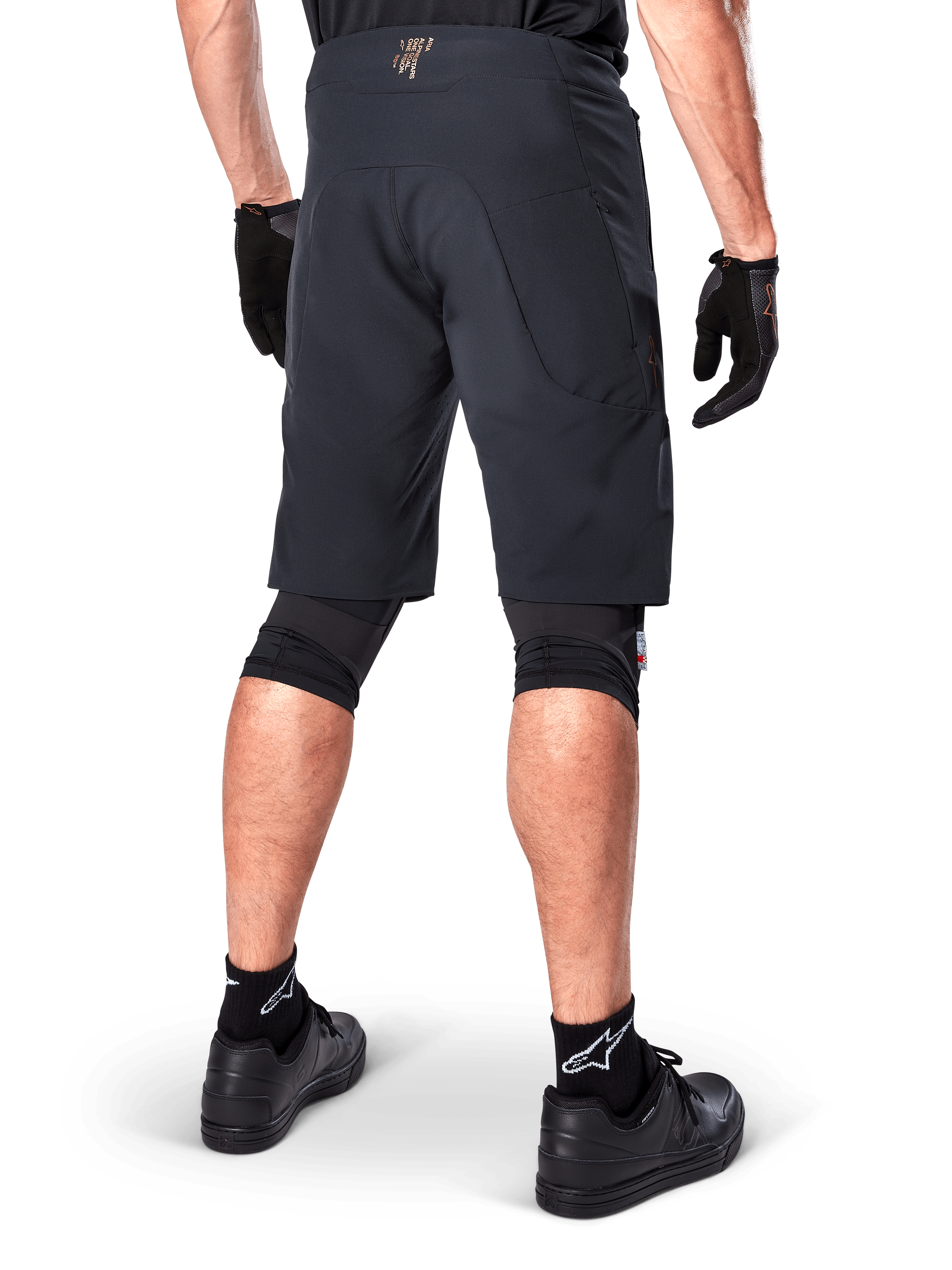 Alpinestars A-Aria Elite Shorts in het zwart, prestatiegerichte mountainbike short, achteraanzicht van een fietser met zwarte fietshandschoenen en zwarte schoenen, ontworpen voor optimale bewegingsvrijheid op off-road trails