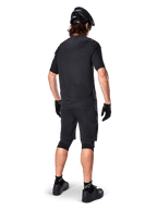 Achteraanzicht van een mountainbiker die Alpinestars A-Aria Elite Shorts in het zwart draagt, gecombineerd met een bijpassende zwarte jersey met korte mouwen, zwarte helm, handschoenen en MTB-schoenen, wat een complete performance-outfit voor off-road fietsen toont.