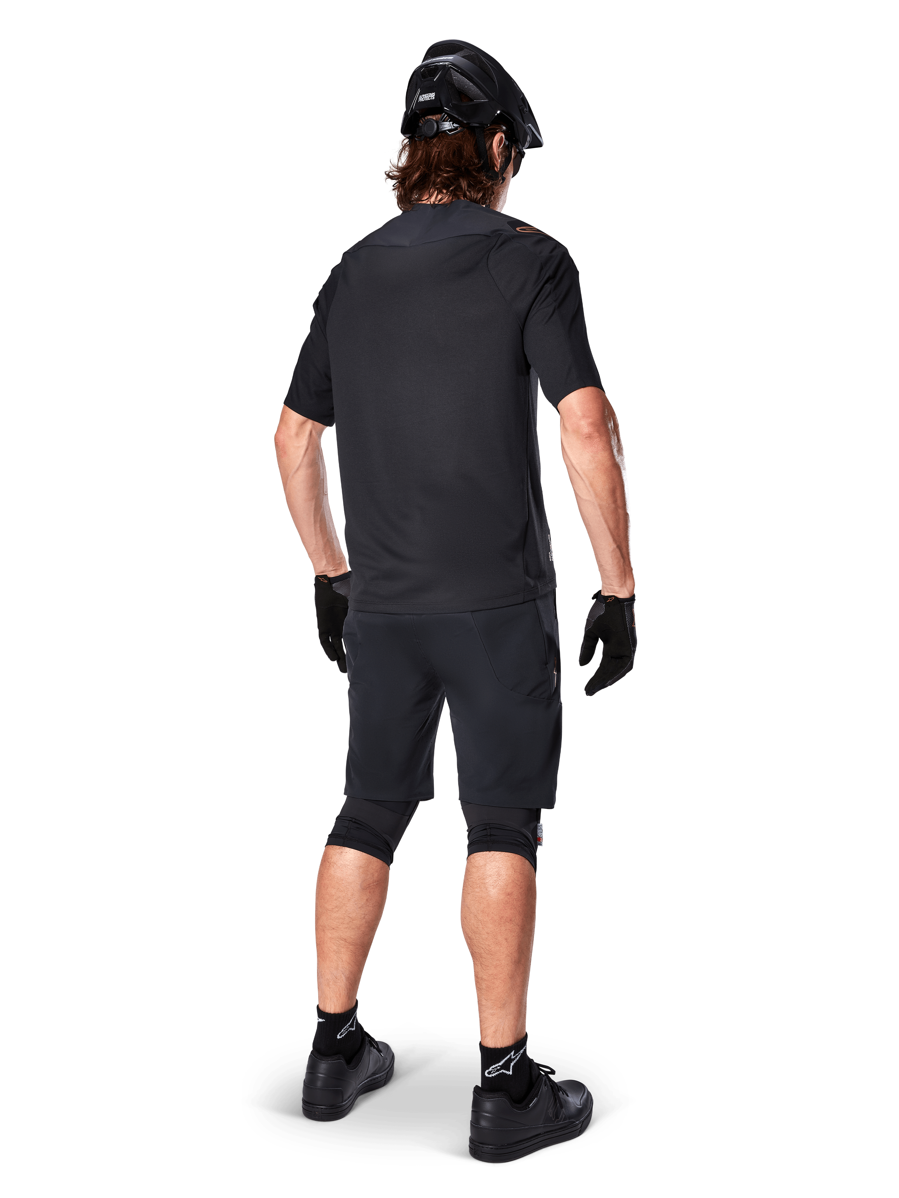 Achteraanzicht van een mountainbiker die Alpinestars A-Aria Elite Shorts in het zwart draagt, gecombineerd met een bijpassende zwarte jersey met korte mouwen, zwarte helm, handschoenen en MTB-schoenen, wat een complete performance-outfit voor off-road fietsen toont.