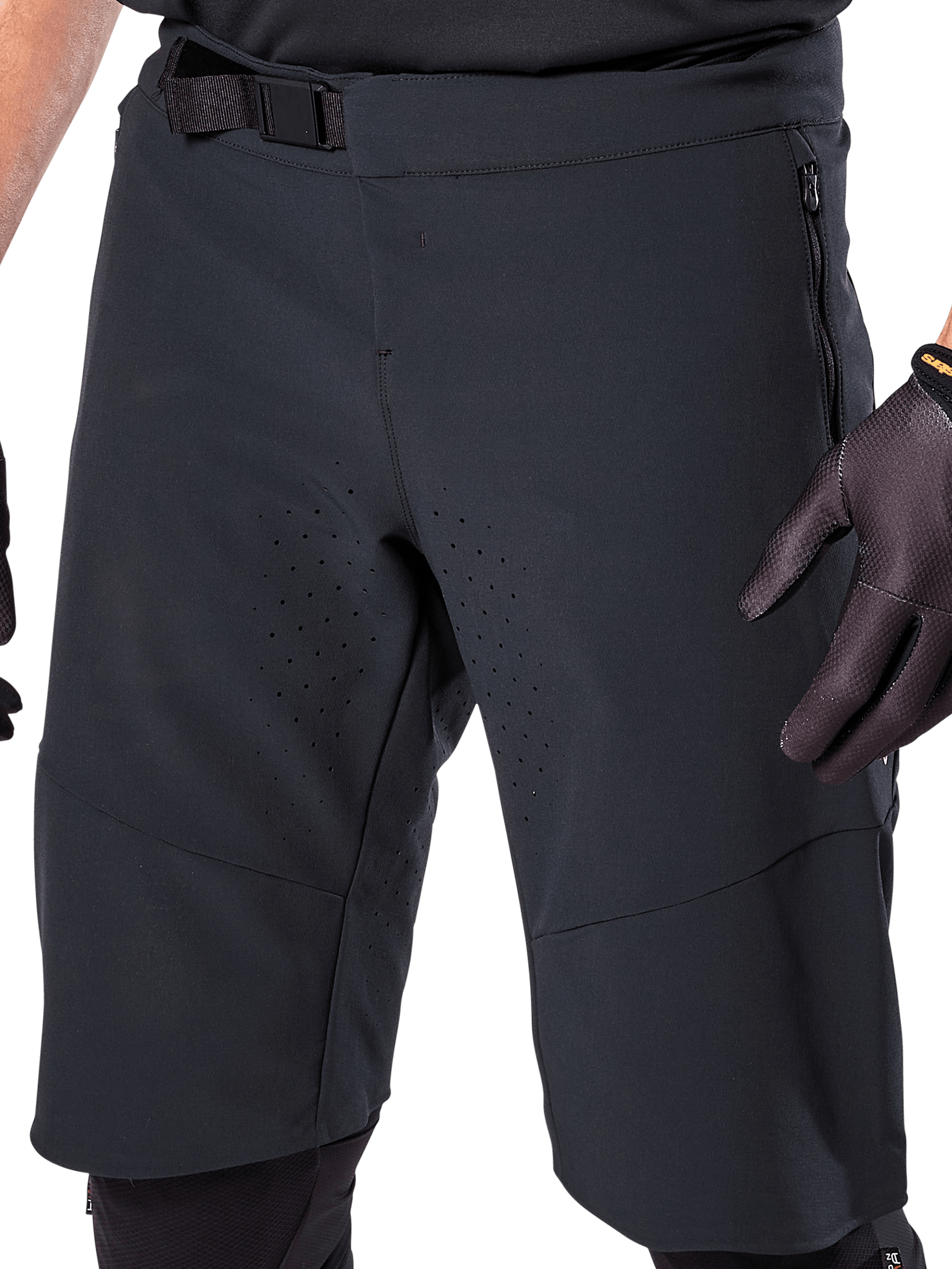 Alpinestars A-Aria Elite Shorts in zwart, close-up van de taille en dij, voorzien van magnetische gespsluiting, zakken met ritssluiting en lasergesneden ventilatieperforaties, gedragen met zwarte fietshandschoenen voor mountainbiken