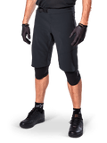 Alpinestars A-Aria Elite Shorts, zwarte mountainbike broek, gedragen met bijpassende zwarte handschoenen en kniebeschermers, voorzien van een magnetische gesp en lasergesneden perforaties, strak ontwerp voor off-road mountainbiken