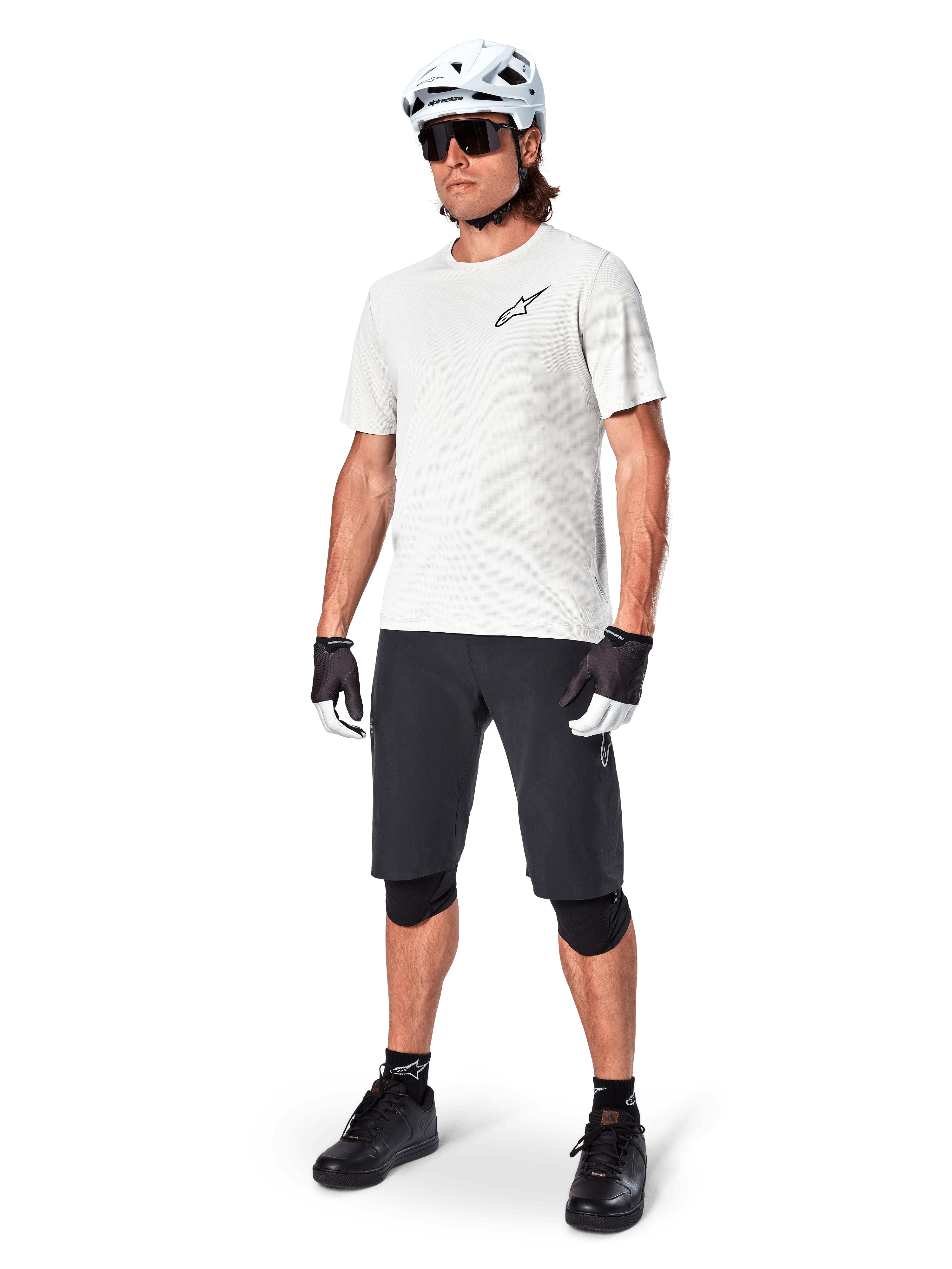 Vététiste homme portant le short Alpinestars A-Aria, short de cyclisme noir, associé à un maillot blanc à manches courtes, un casque de VTT blanc et un équipement technique noir, tenue complète pour la pratique du VTT tout-terrain