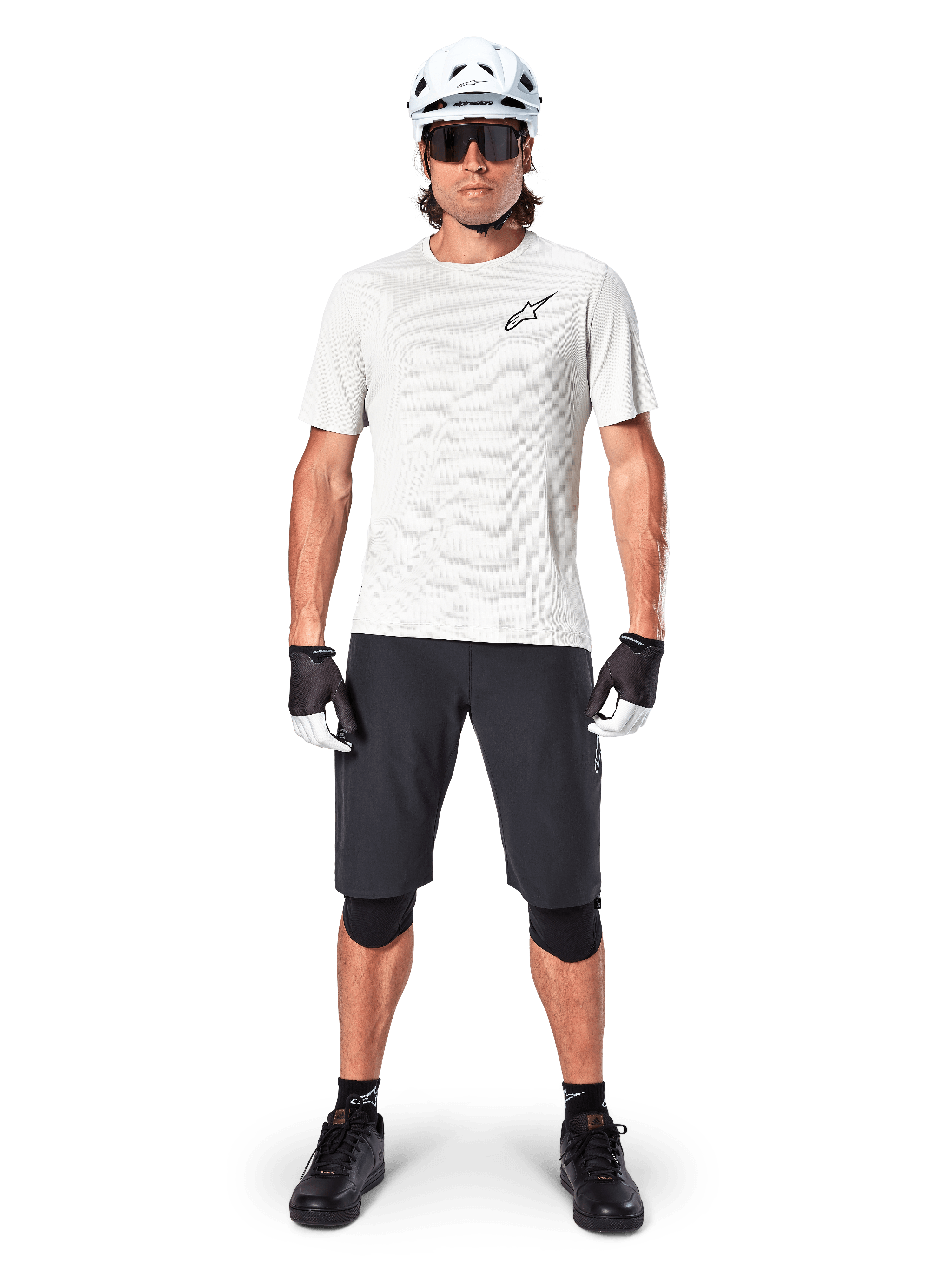 Vététiste homme portant le short Alpinestars A-Aria Noir, associé à un maillot technique blanc, un casque blanc et des protège-genoux noirs, équipement de cyclisme tout-terrain professionnel, vue de face complète