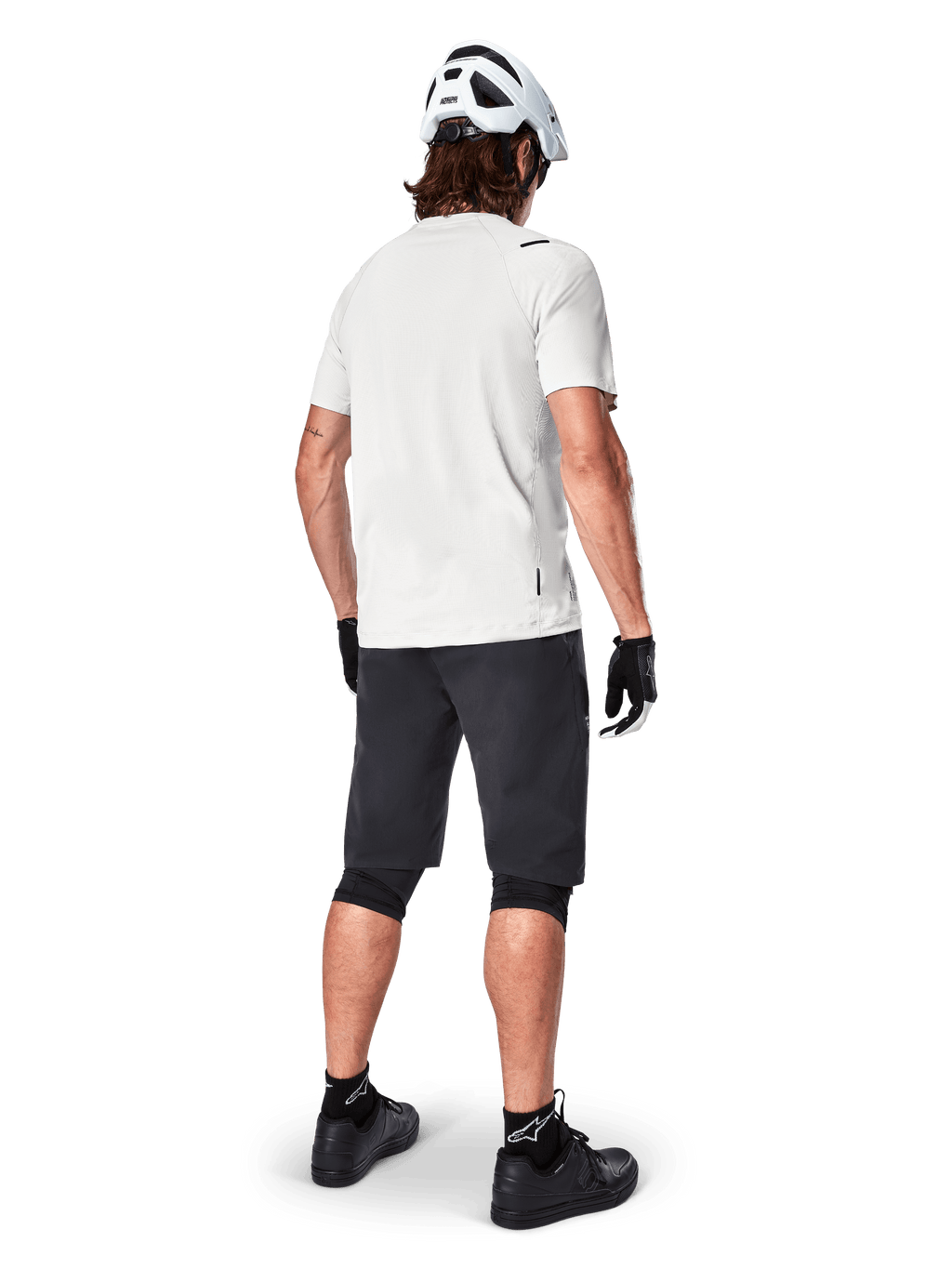 Vététiste de dos portant le short Alpinestars A-Aria noir, maillot de performance blanc à manches courtes, casque blanc, gants noirs et chaussures de VTT noires, équipement de cyclisme pour le trail