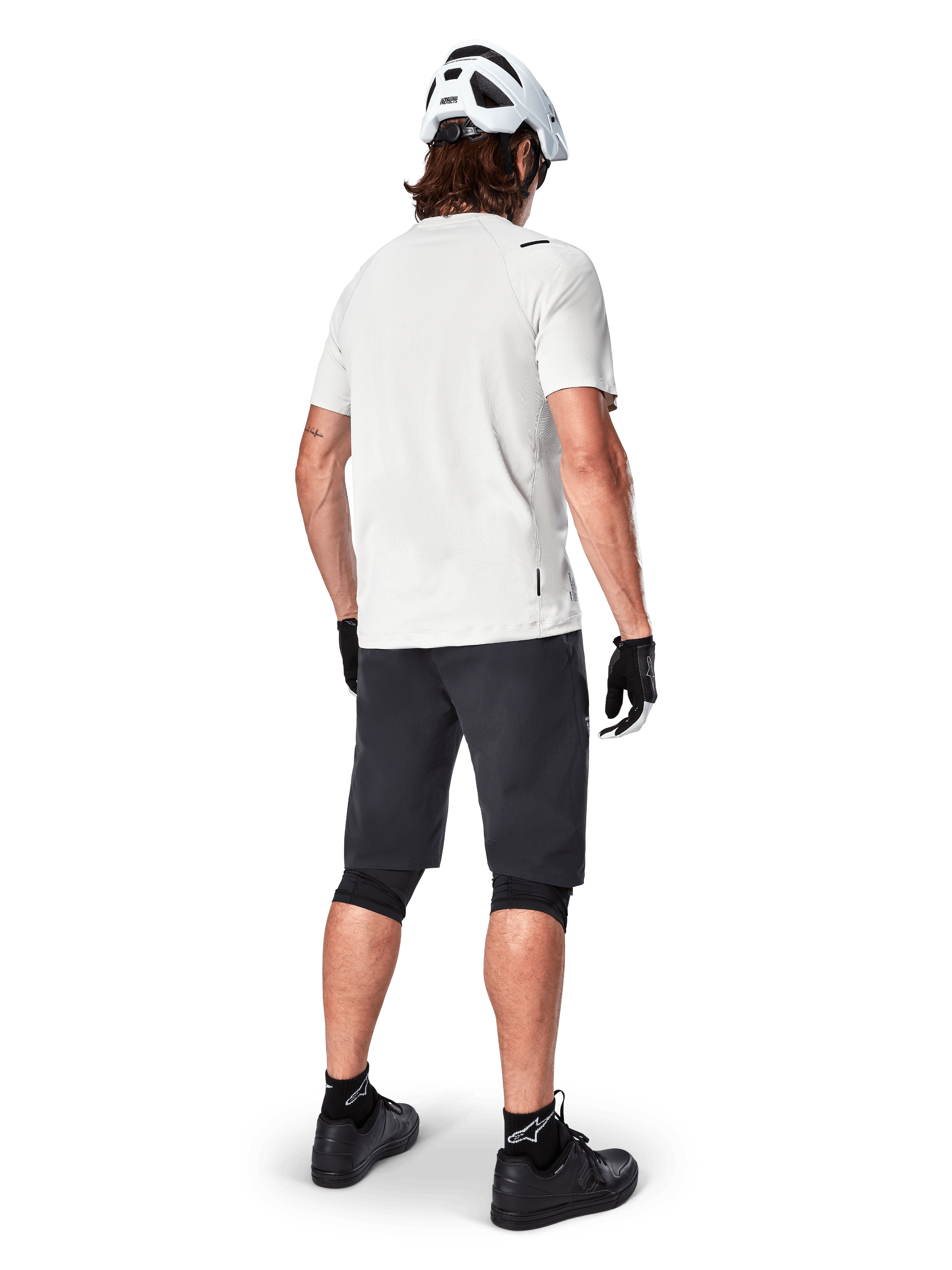 Vététiste de dos portant le short Alpinestars A-Aria noir, maillot de performance blanc à manches courtes, casque blanc, gants noirs et chaussures de VTT noires, équipement de cyclisme pour le trail