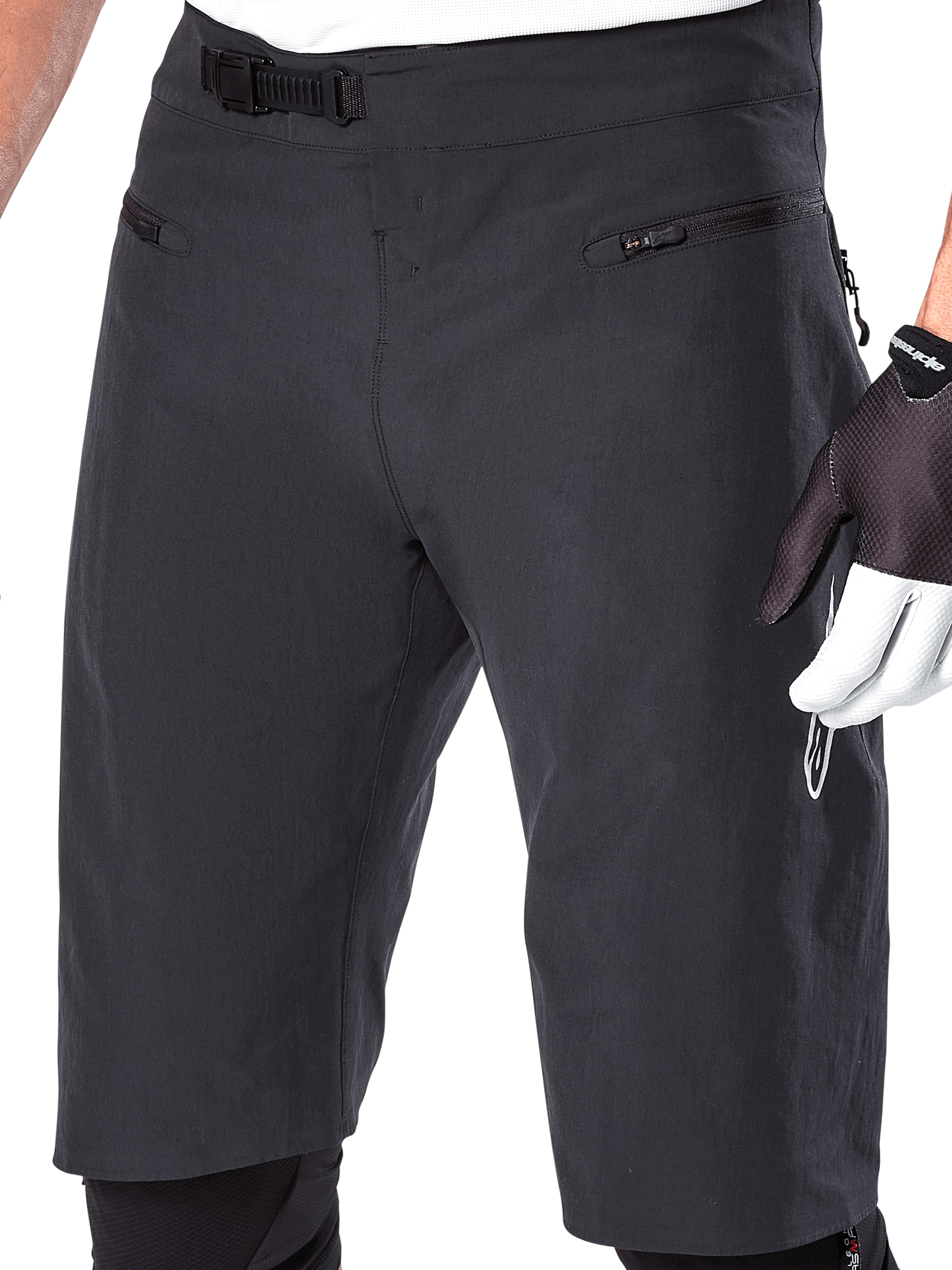 Short Alpinestars A-Aria, short de VTT, noir, vue rapprochée de la taille et des cuisses montrant le système de fermeture à rochet et les poches zippées, porté avec des gants de cyclisme noirs et blancs, équipement de performance pour le trail