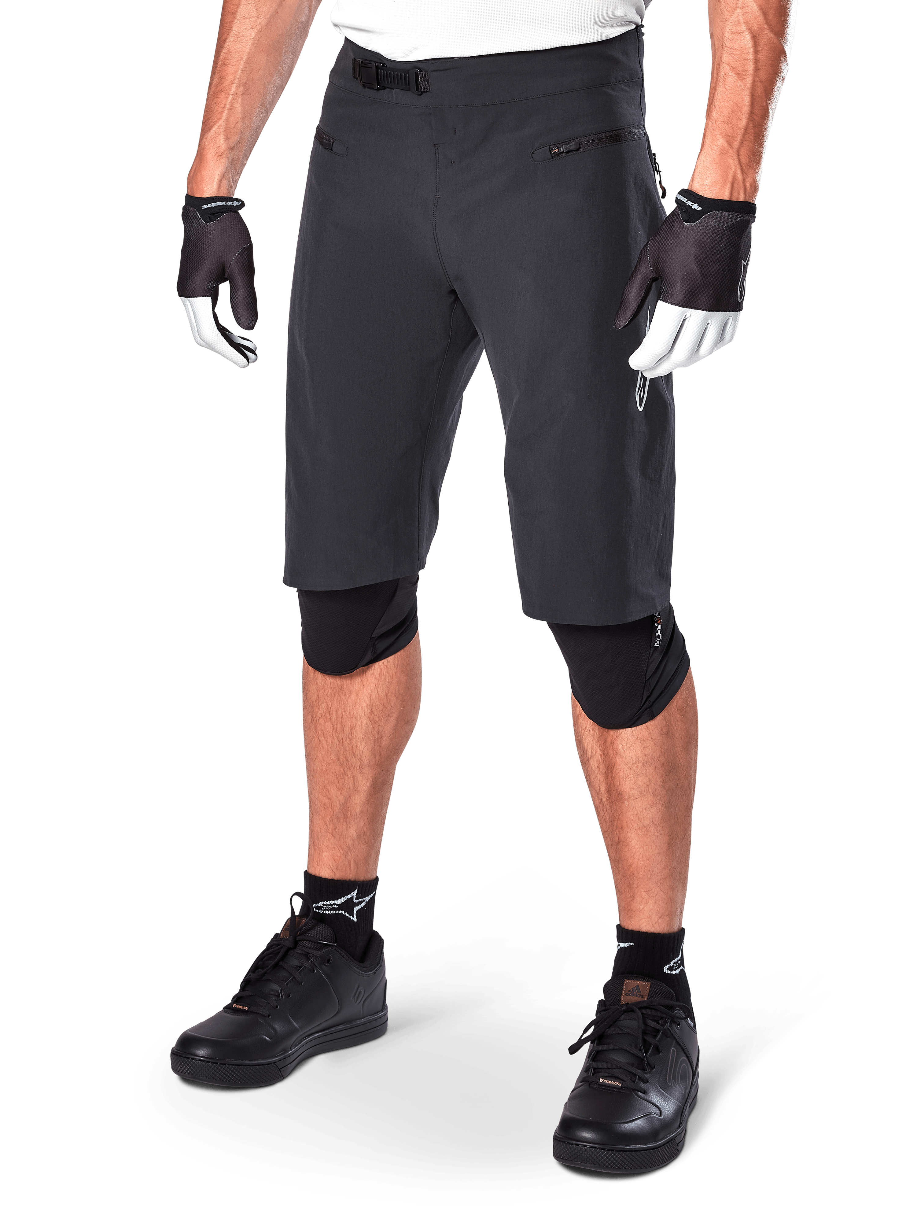 Alpinestars A-Aria Shorts, short de VTT noir, longueur genou avec poches avant zippées et boucle de taille à cliquet réglable, porté avec des genouillères noires, des chaussettes et des gants de cyclisme