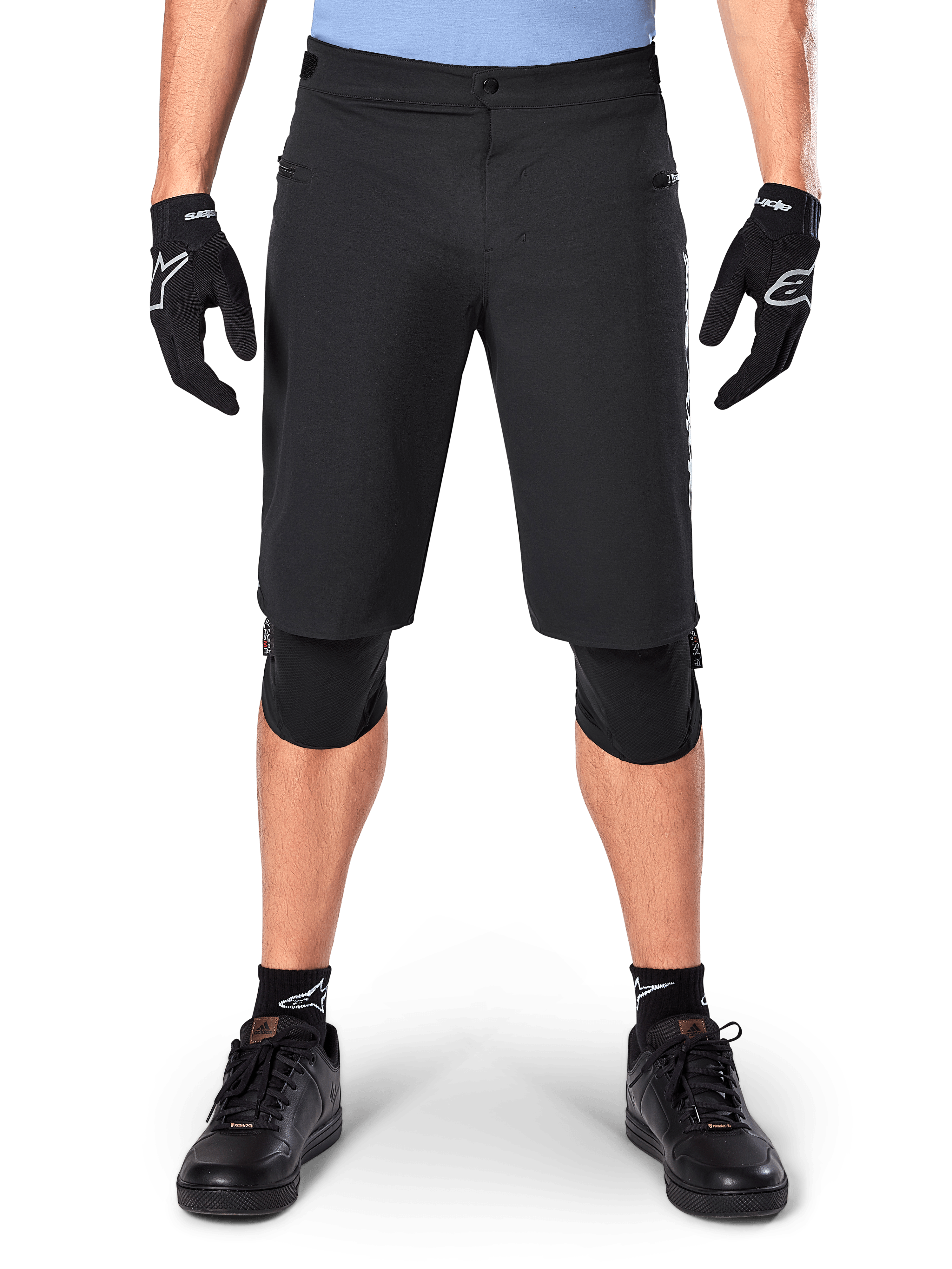Shorts Alpinestars A-Dura Elite, short de VTT noir, porté par un cycliste avec des gants noirs et des genouillères, doté d'une fermeture à bouton-pression à l'avant et de poches zippées, matériau Cordura durable pour le cyclisme tout-terrain