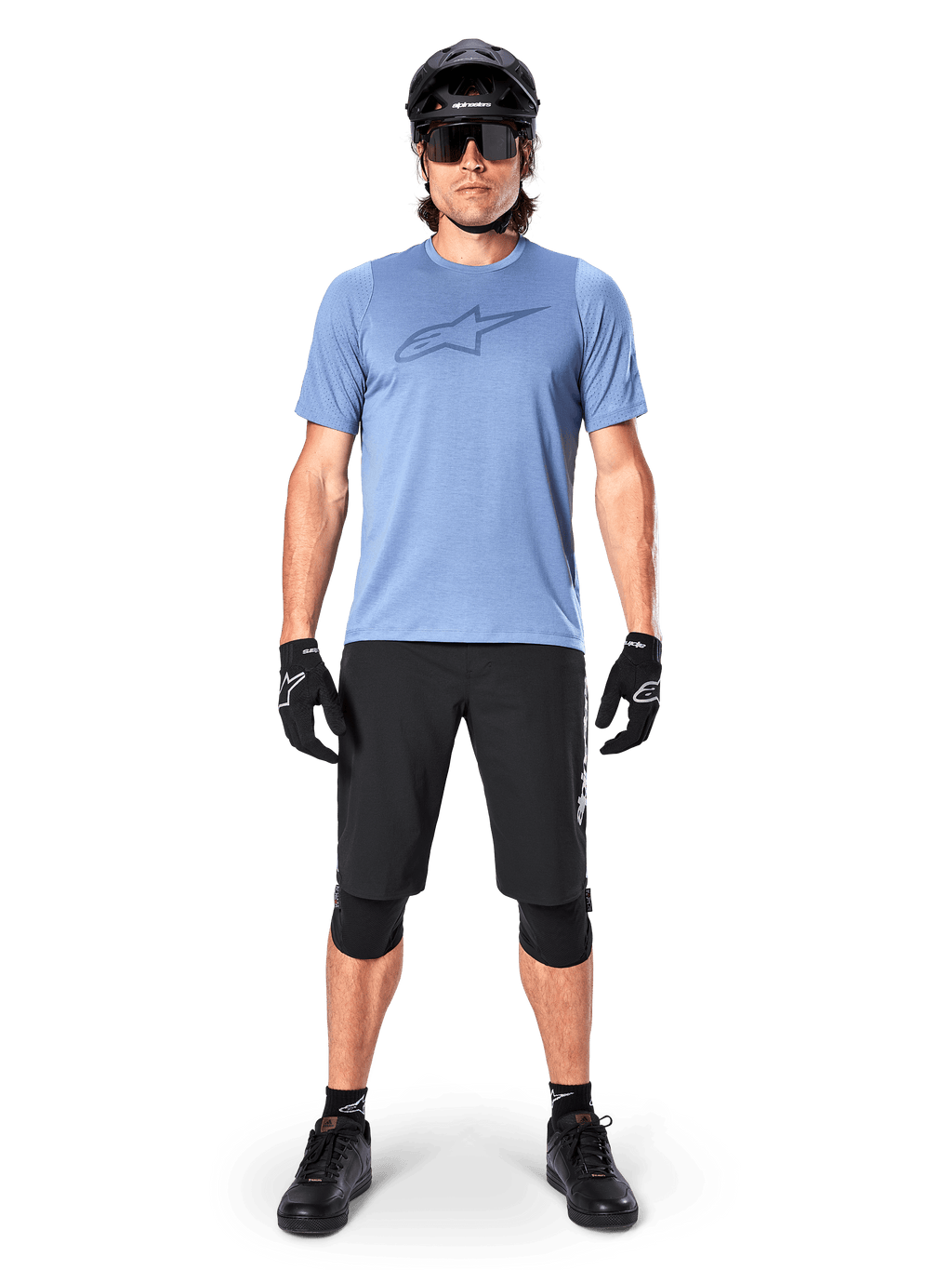 Short Alpinestars A-Dura Elite, short de VTT noir, porté avec un t-shirt bleu clair, un casque noir, des lunettes de soleil et des genouillères, tenue de cyclisme tout-terrain professionnelle
