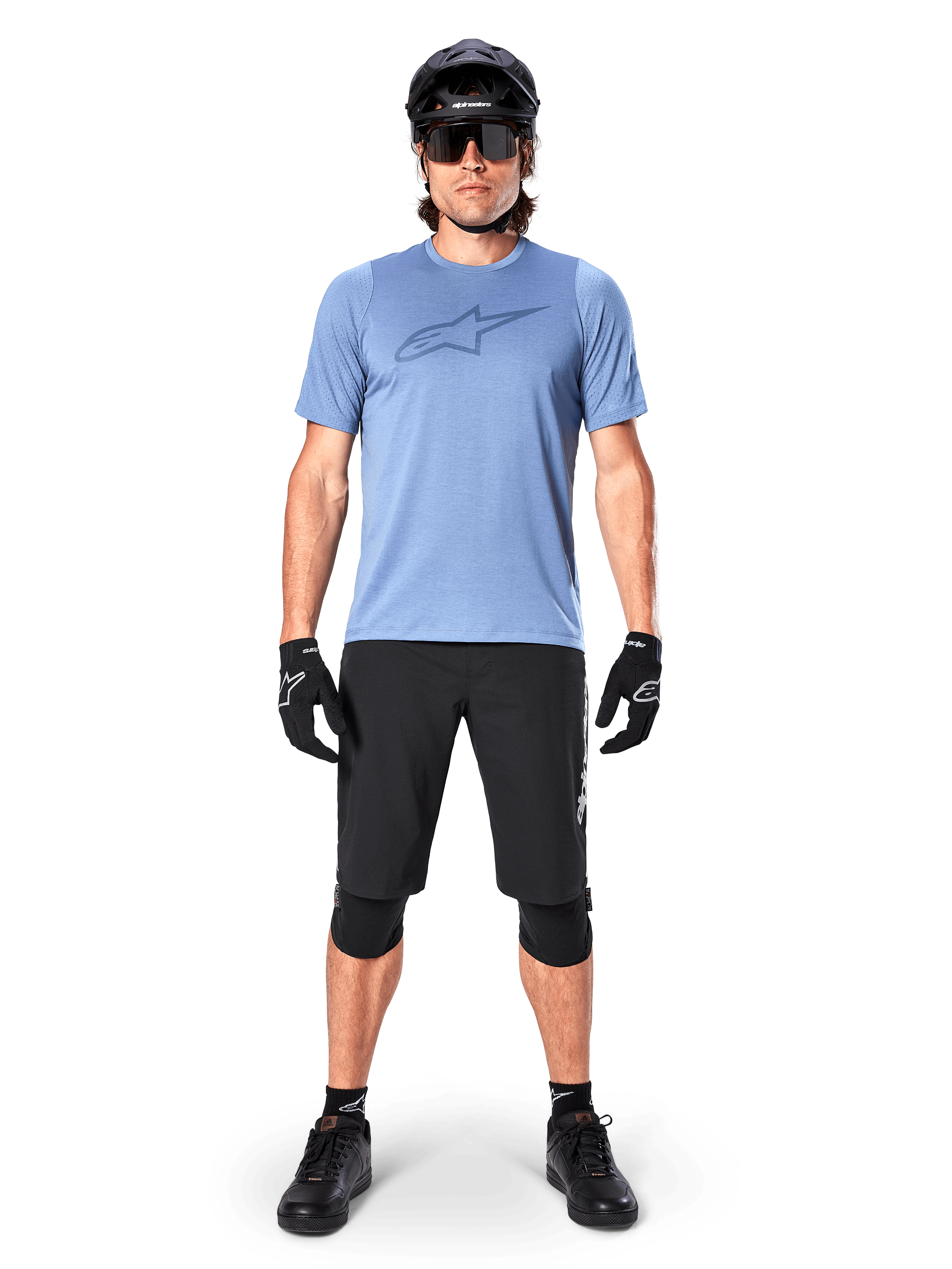 Short Alpinestars A-Dura Elite, short de VTT noir, porté avec un t-shirt bleu clair, un casque noir, des lunettes de soleil et des genouillères, tenue de cyclisme tout-terrain professionnelle