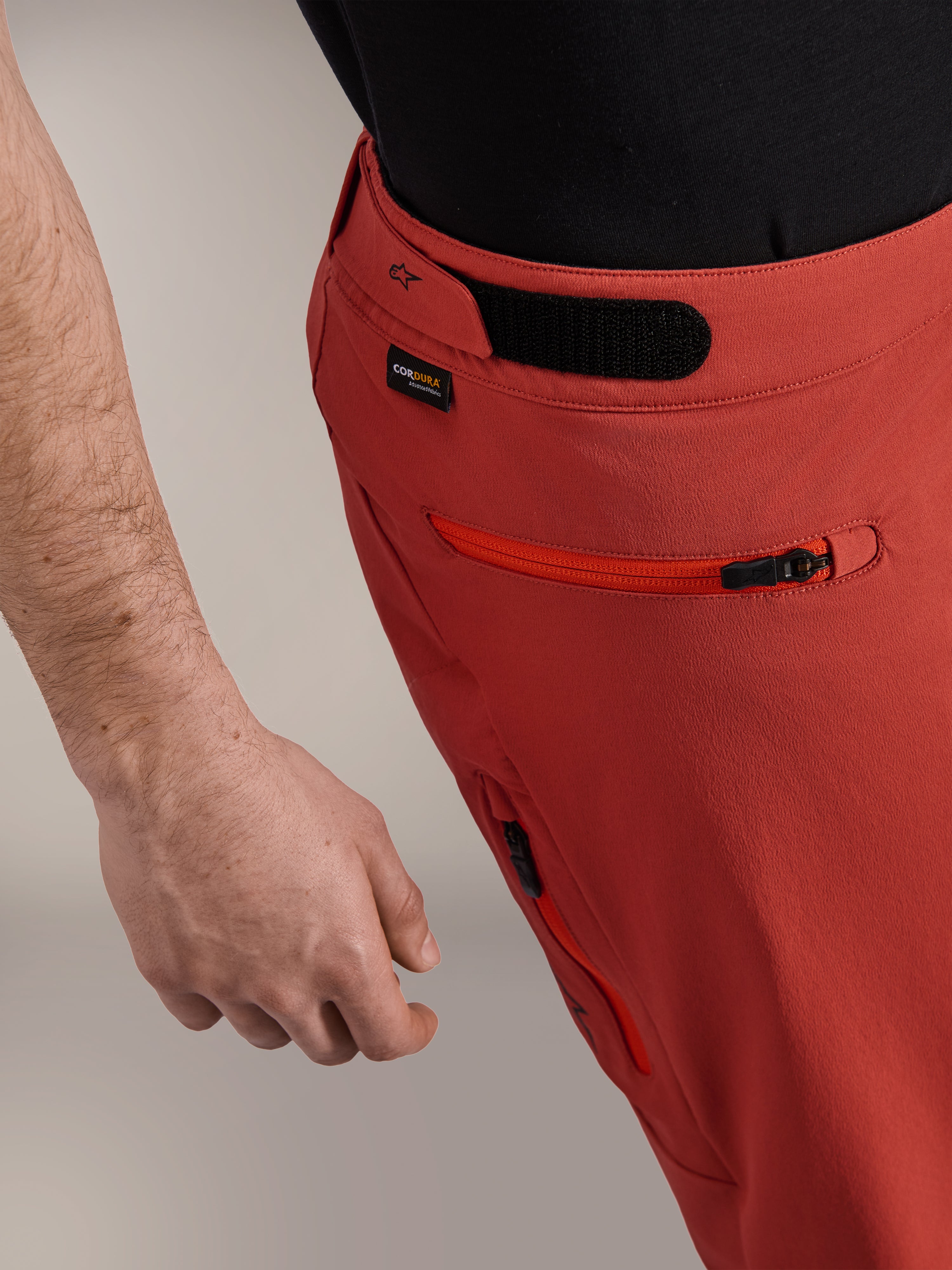 Alpinestars A-Dura Elite Shorts, Dunkelorange, Nahaufnahme des Seitenprofils mit Haken- und Schlaufen-Seitenversteller, Cordura®-Logo und Seitentasche mit Reißverschluss, Premium-Mountainbike-Shorts.