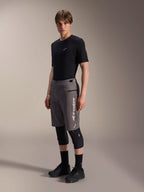 Alpinestars A-Dura Elite Shorts, dunkelgraue Mountainbike-Shorts, von einem Model mit schwarzem T-Shirt und Knieschützern getragen, mit vertikalem weißem Alpinestars-Logo auf dem linken Bein, technisches Cordura-Gewebe für Offroad-Radsport