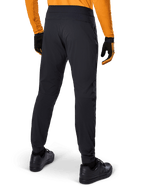 Alpinestars A-Dura Pants, zwarte MTB-broek, achteraanzicht, gedragen met een oranje jersey met lange mouwen en zwarte handschoenen, voorzien van elastische manchetten en duurzaam textielmateriaal voor mountainbiken