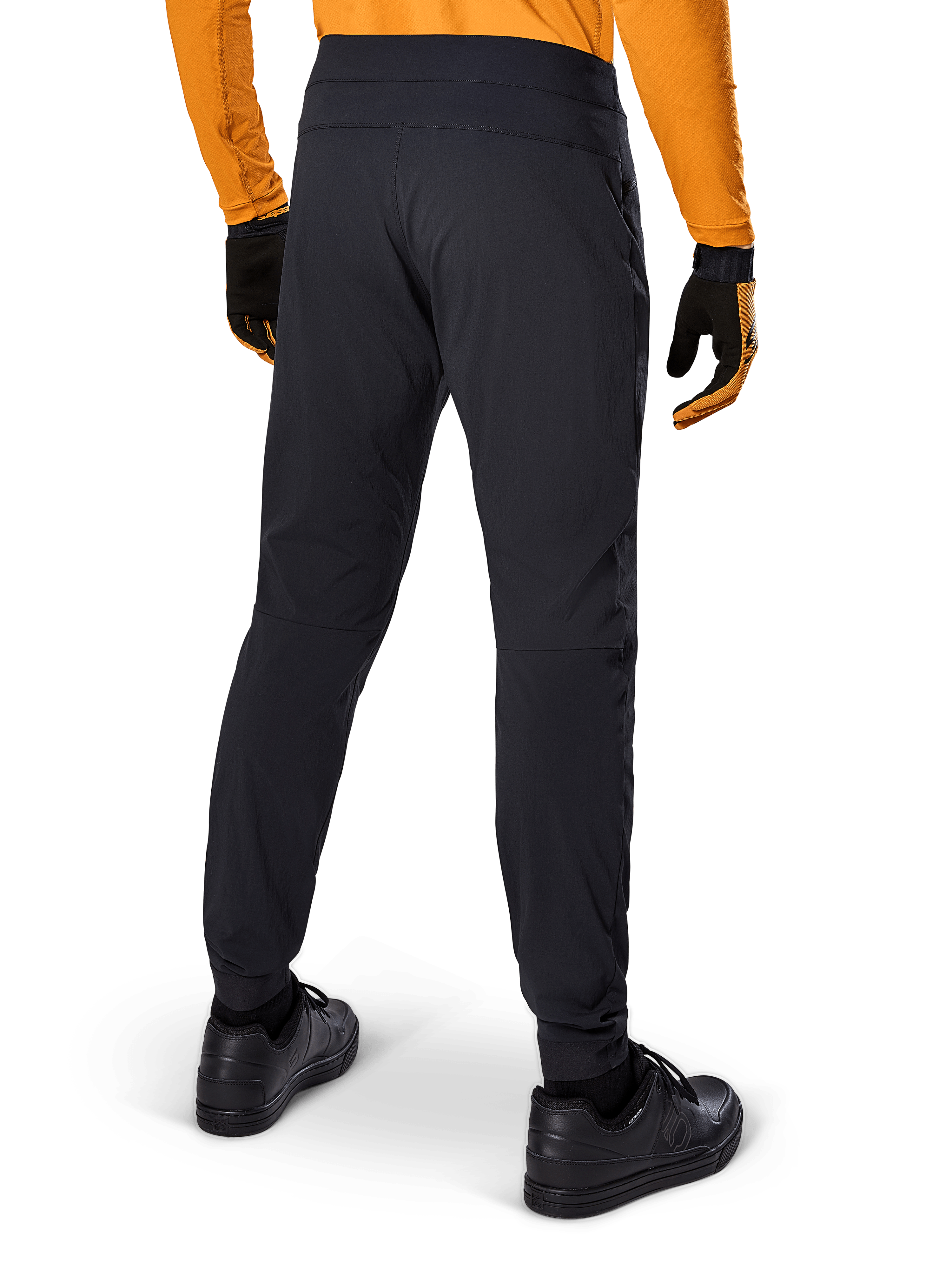 Alpinestars A-Dura Pants, zwarte MTB-broek, achteraanzicht, gedragen met een oranje jersey met lange mouwen en zwarte handschoenen, voorzien van elastische manchetten en duurzaam textielmateriaal voor mountainbiken