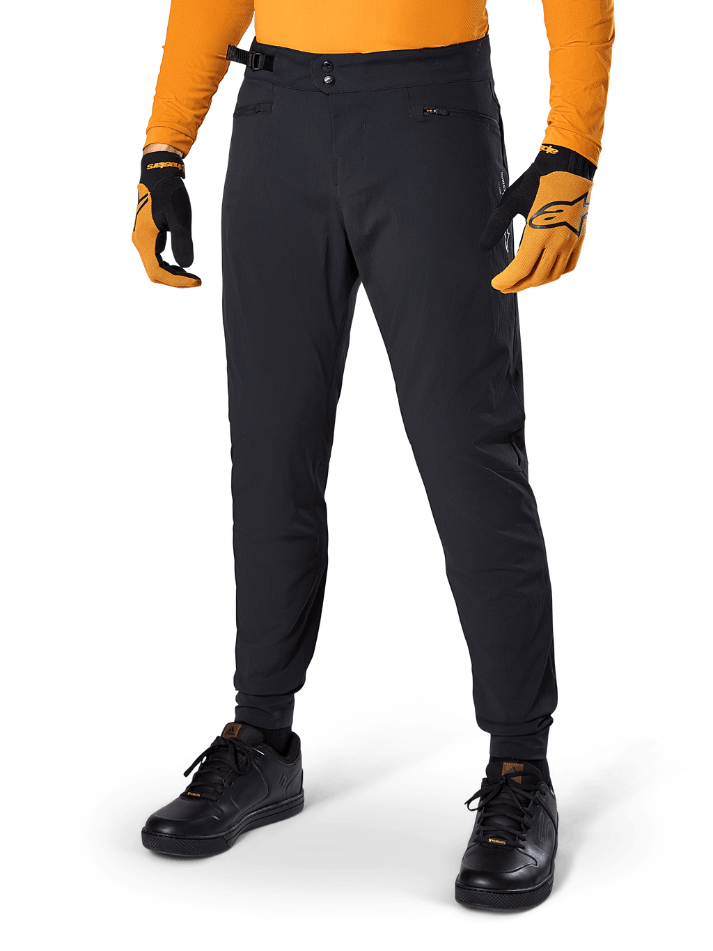 Alpinestars A-Dura Pants, mountainbikebroek, zwart, met zijsluitingen en zakken met rits, gedragen met oranje jersey en handschoenen, sportieve regular fit voor mountainbiken